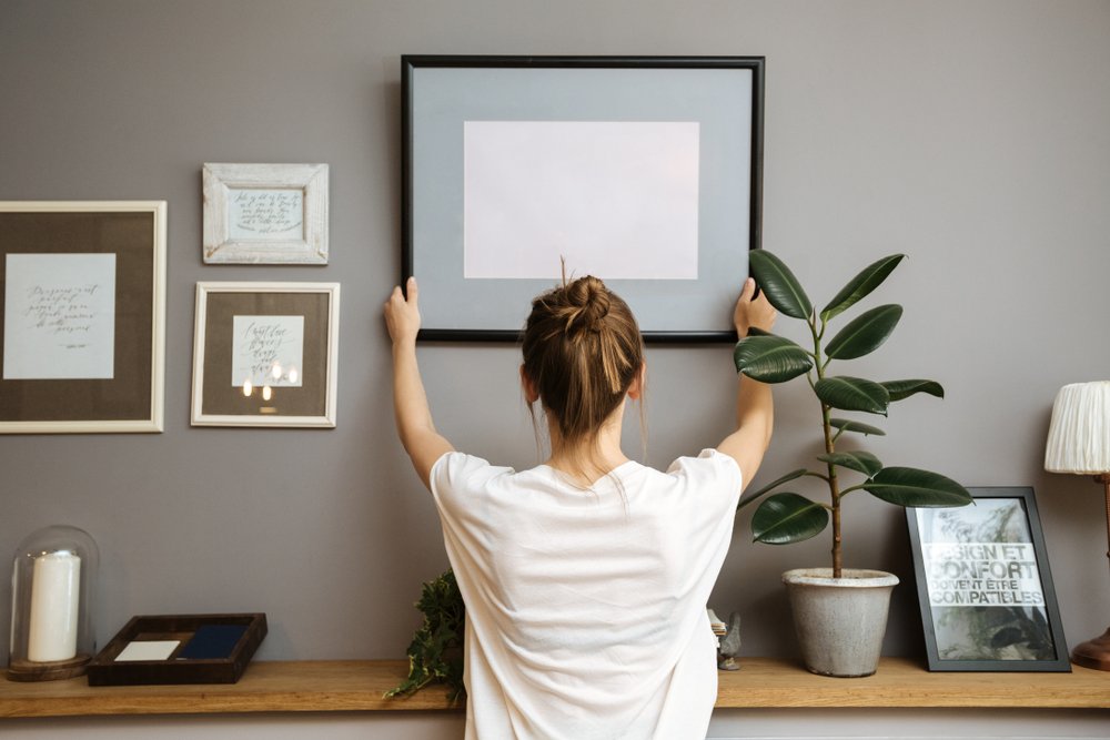 Woman hanging a frame on a gray wall | Photo: Shutterstock/Igor_Kravtsov