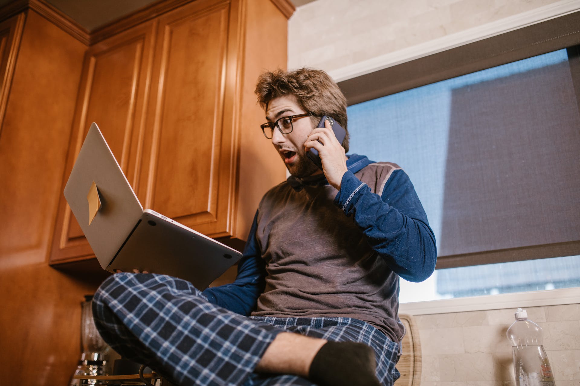 A surprised man looking at his laptop while talking on his phone | Source: Pexels