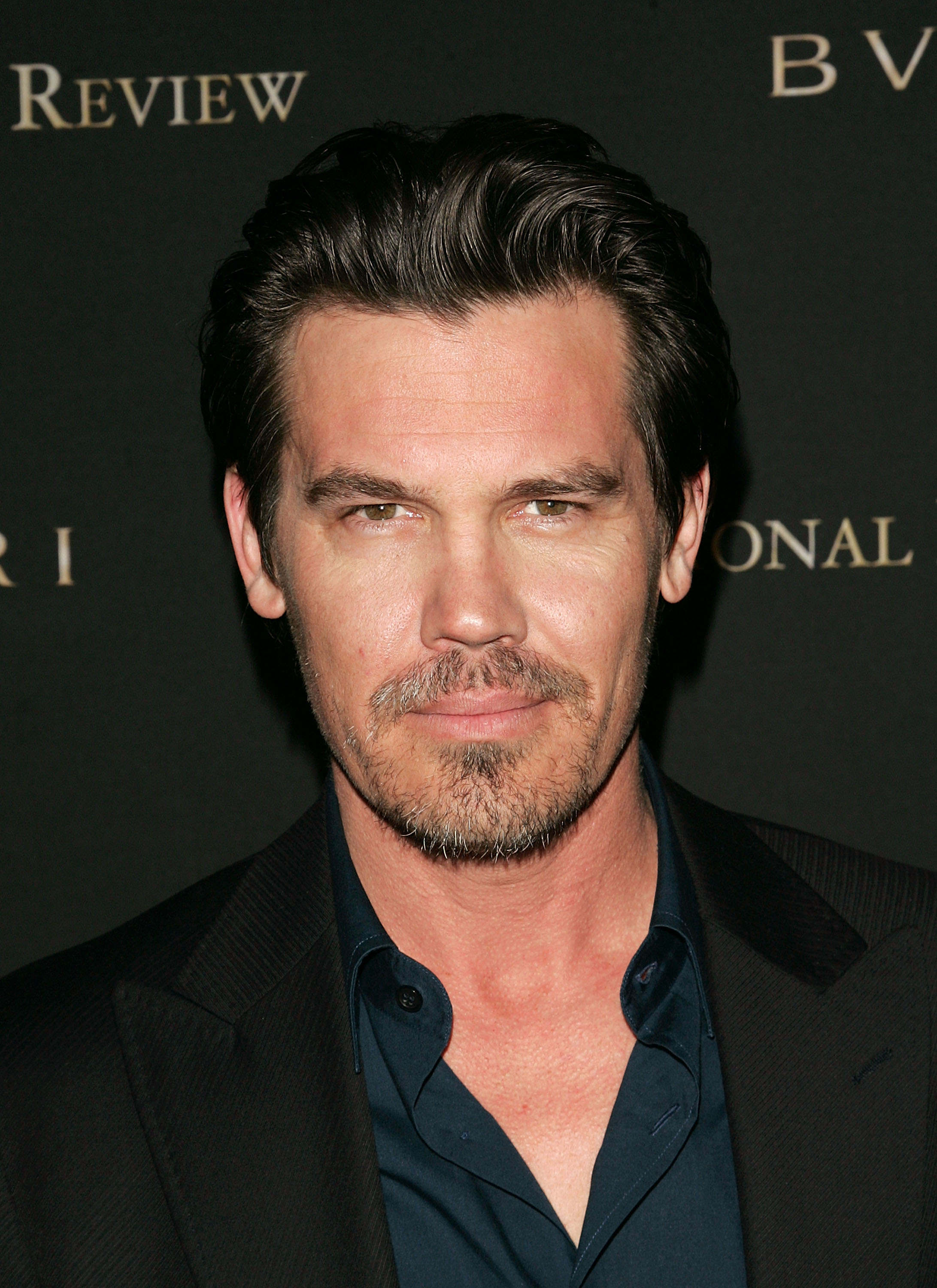 Wearing a dark open-collar shirt and a pinstriped jacket, he appears with a short beard and slightly graying stubble, the start of a more rugged, weathered look that would define his next era.