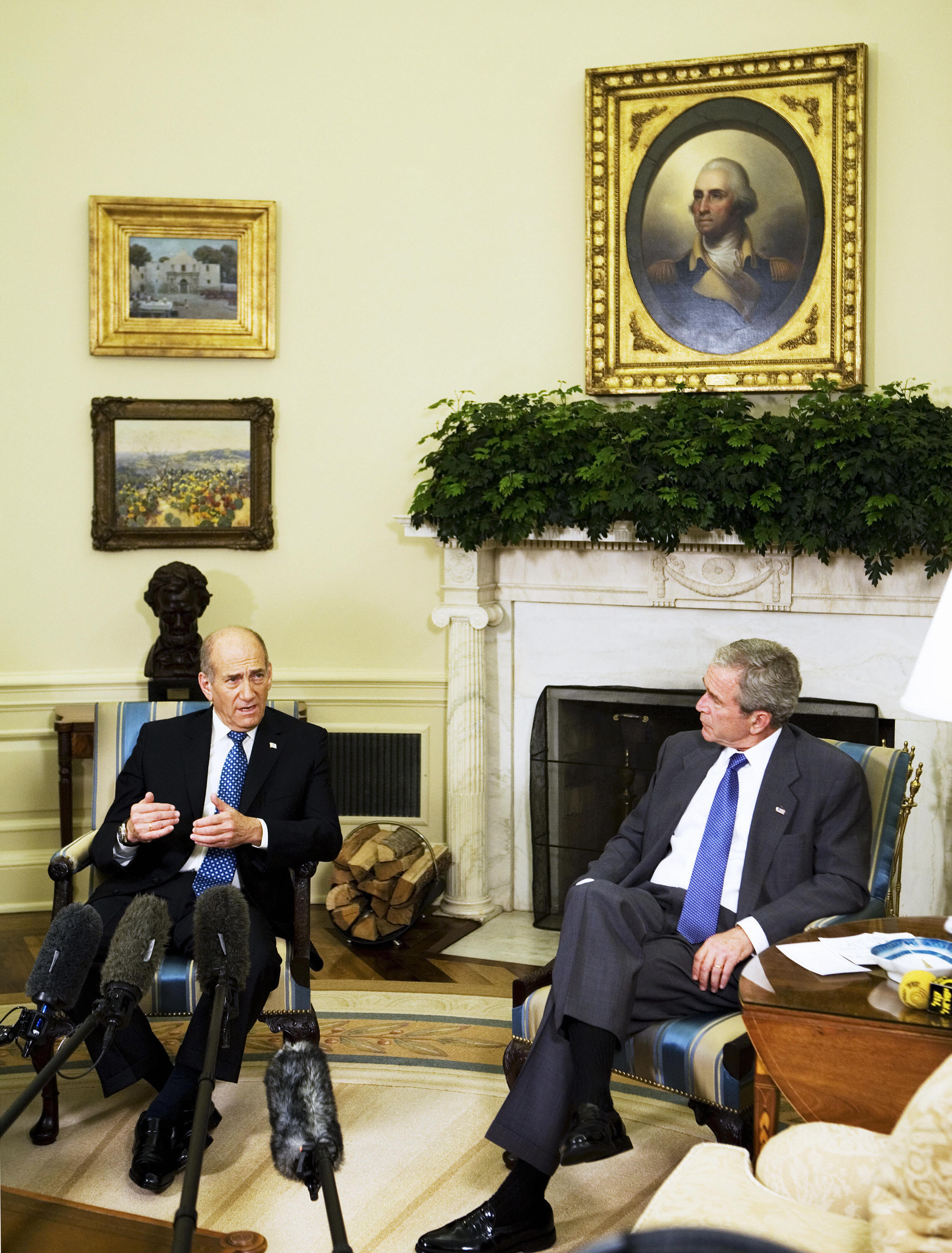 George W. Bush meets Israeli Prime Minister Ehud Olmert in the Oval Office on June 19, 2007, where potted greenery, classic paintings, and a wood-stacked fireplace set a formal scene.