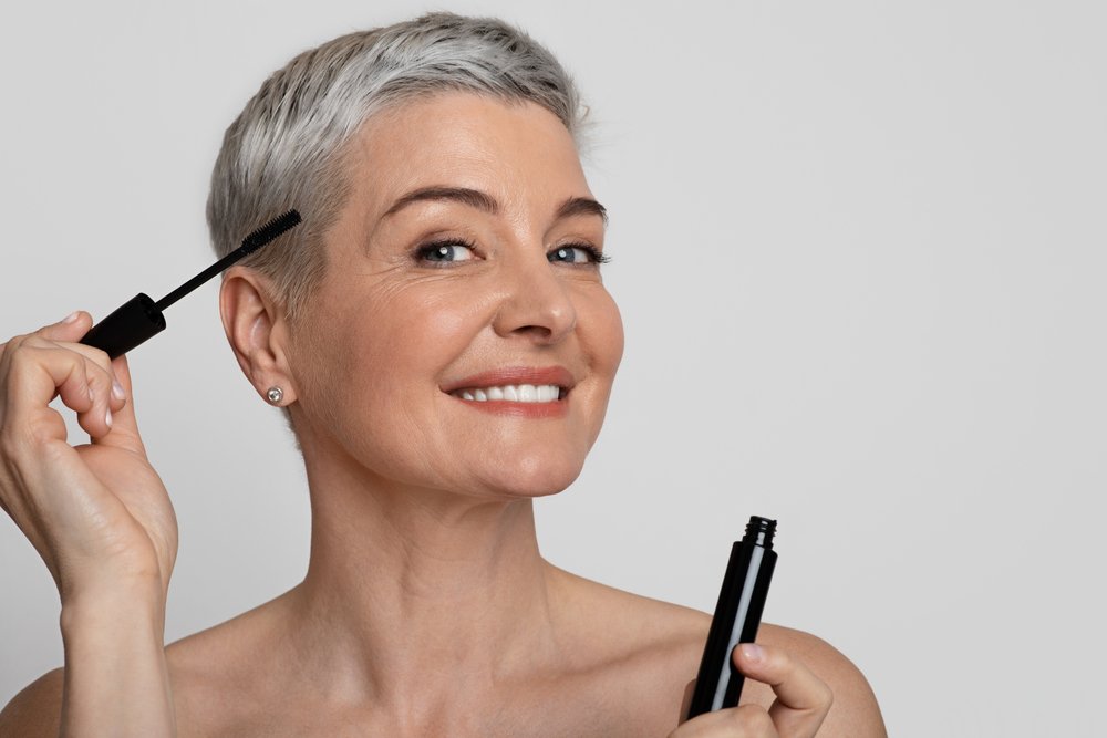 Retrato de una mujer madura sonriente aplicándose rímel. | Foto: Shutterstock