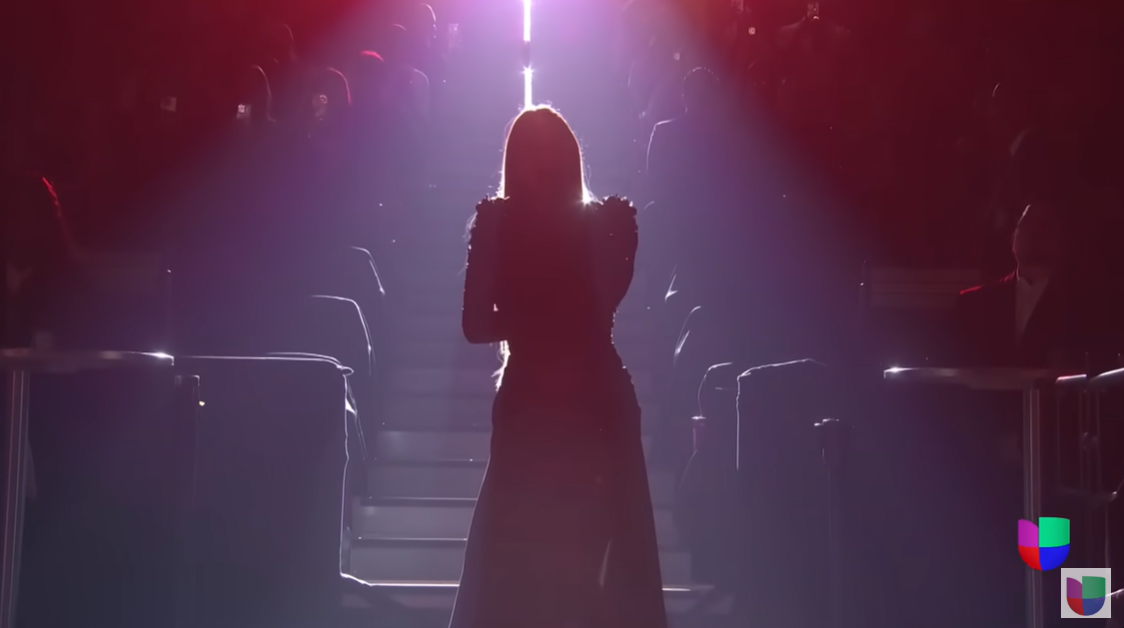 India Martínez descends an illuminated staircase, framed by dramatic backlighting as she opens the performance, posted on February 22, 2025 | Source: YouTube/univision