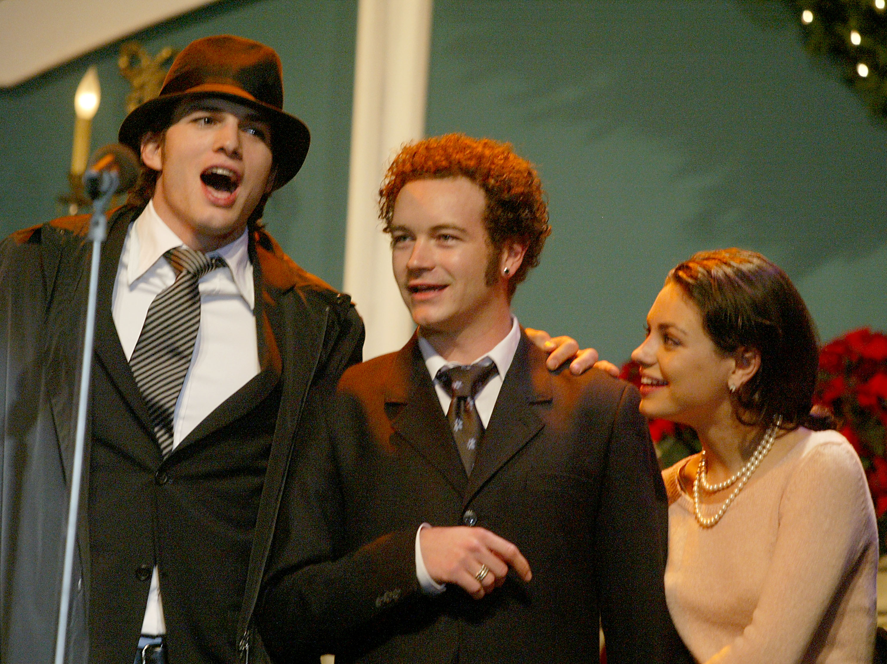 (L-R) Ashton Kutcher, Danny Masterson and Mila Kunis perform on stage at the Church of Scientology's 11th Annual Christmas Stories Fundraiser on December 6, 2003 in Los Angeles, California | Source: Getty Images