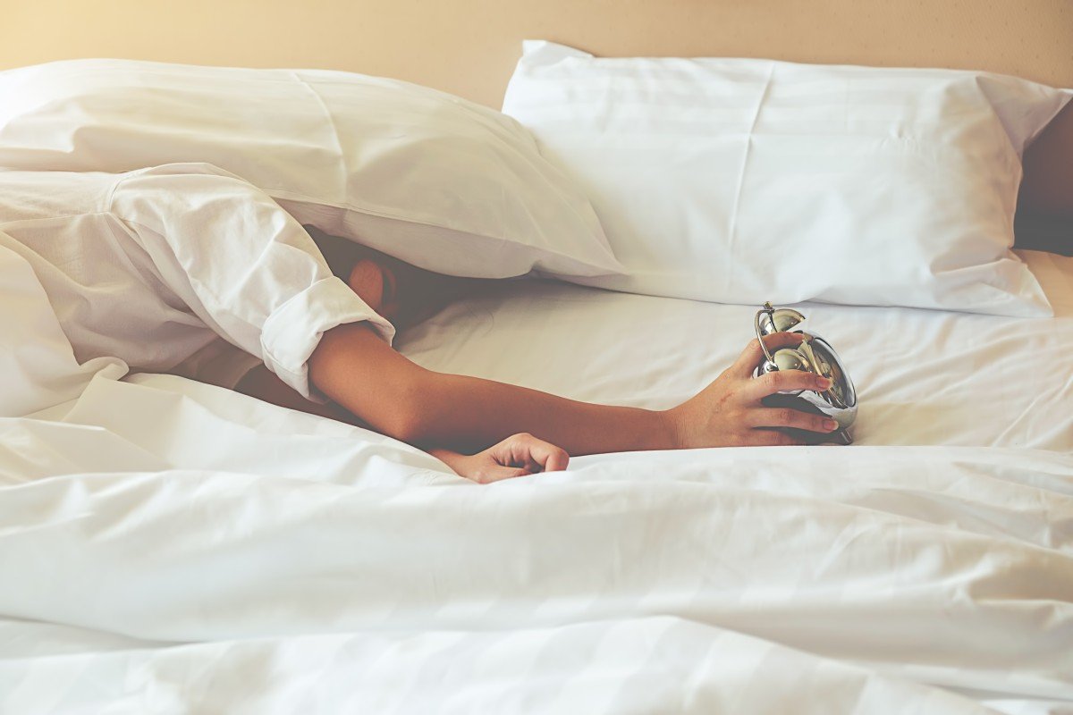 Mujer acostada en una cama mientras sostiene un despertador. | Foto: PxHere