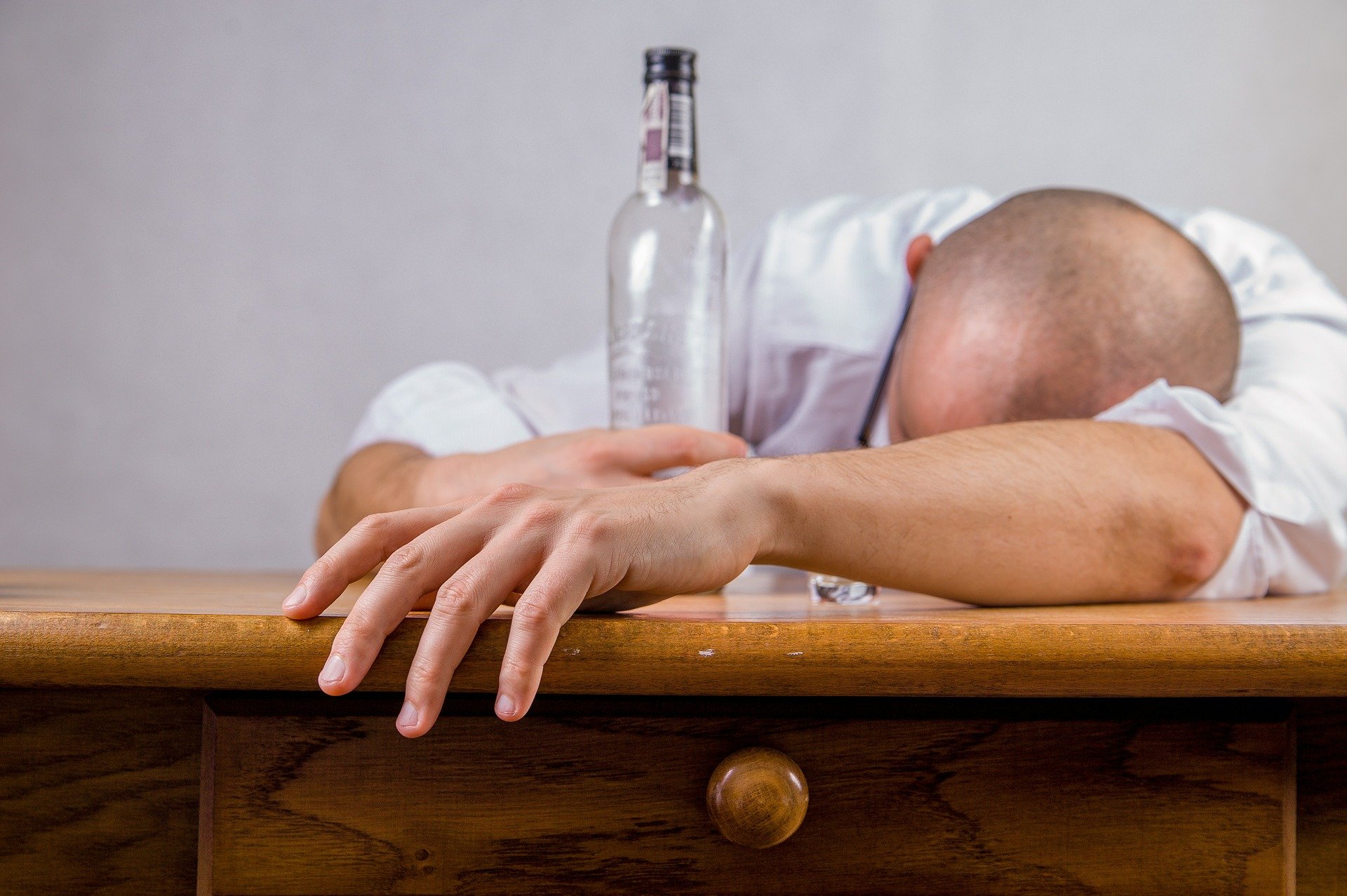 A drunk man lying on a table sleeping while holding on to an alcohol bottle | Photo: Pixabay/Michal Jarmoluk