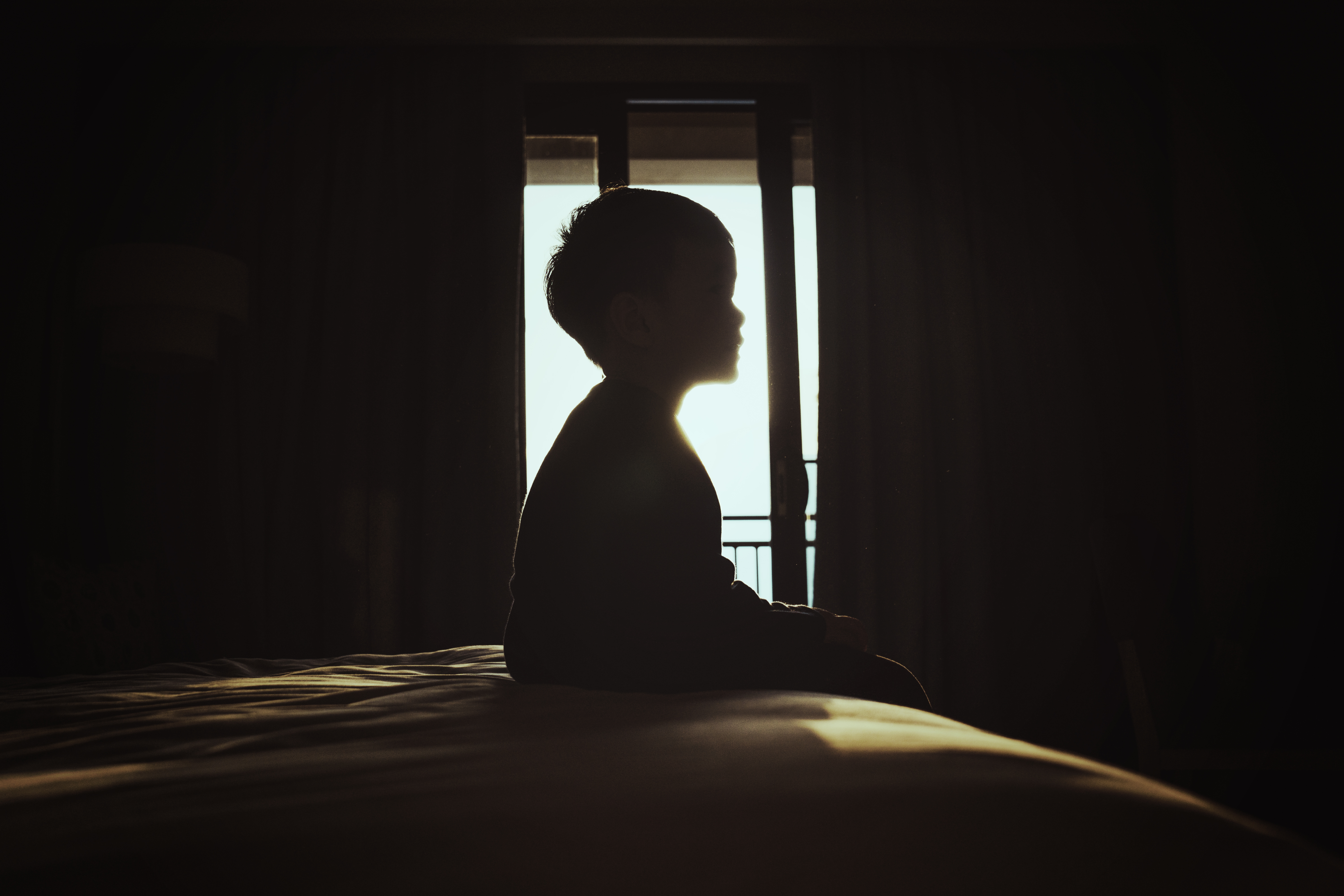 Silhouette of a boy sitting on a bed | Source: Getty Images