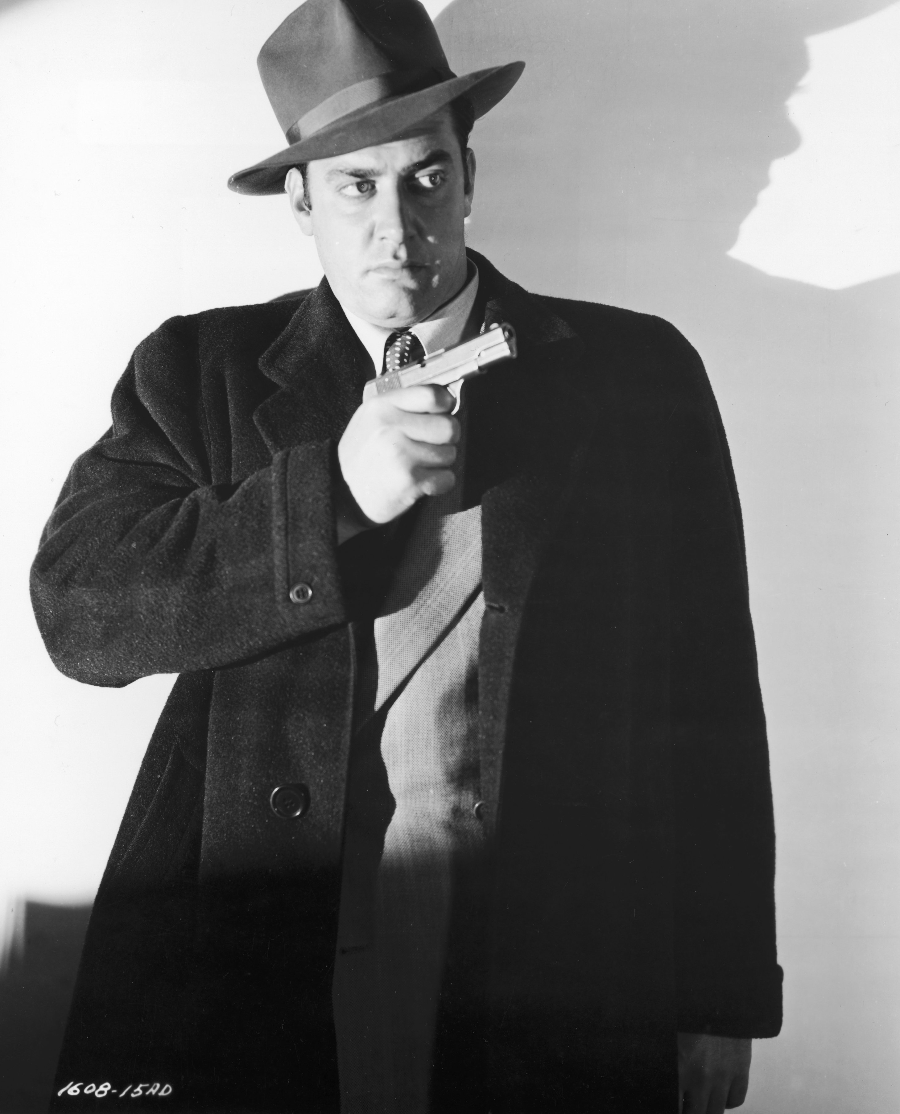 Raymond Burr (1917 - 1993), wearing a hat and an overcoat, holds a gun in a still from director Joseph Newman's film, 'Abandoned.' | Source: Getty Images