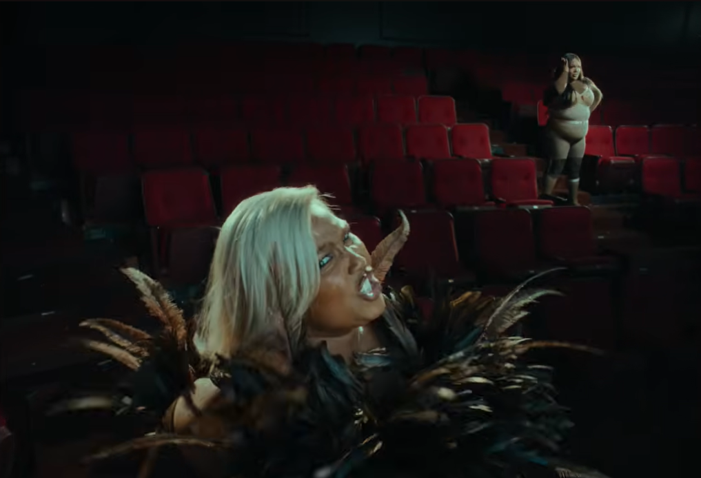 A stage sequence shows Lizzo in a dramatic feathered outfit as her alter ego takes over the performance from a distance | Source: YouTube/Lizzo