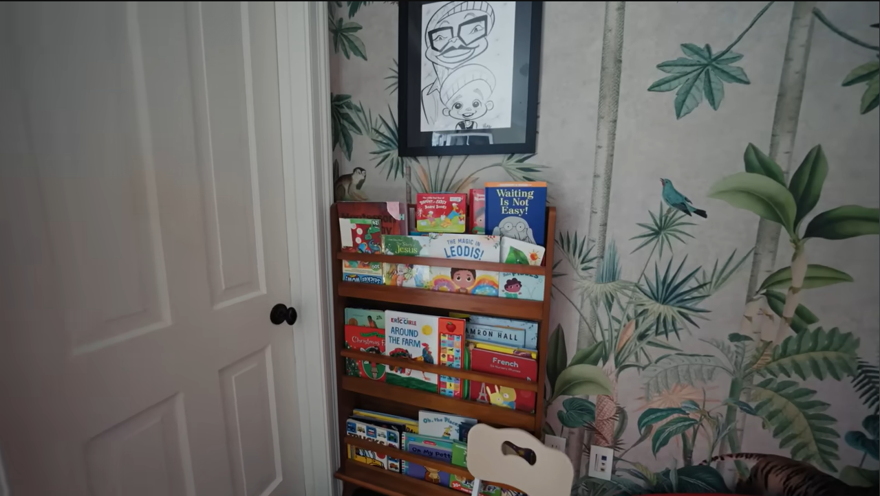 A closer look at the bookshelf, complete with childhood classics and a custom framed drawing hanging above. | Source: YouTube/@Archdigest