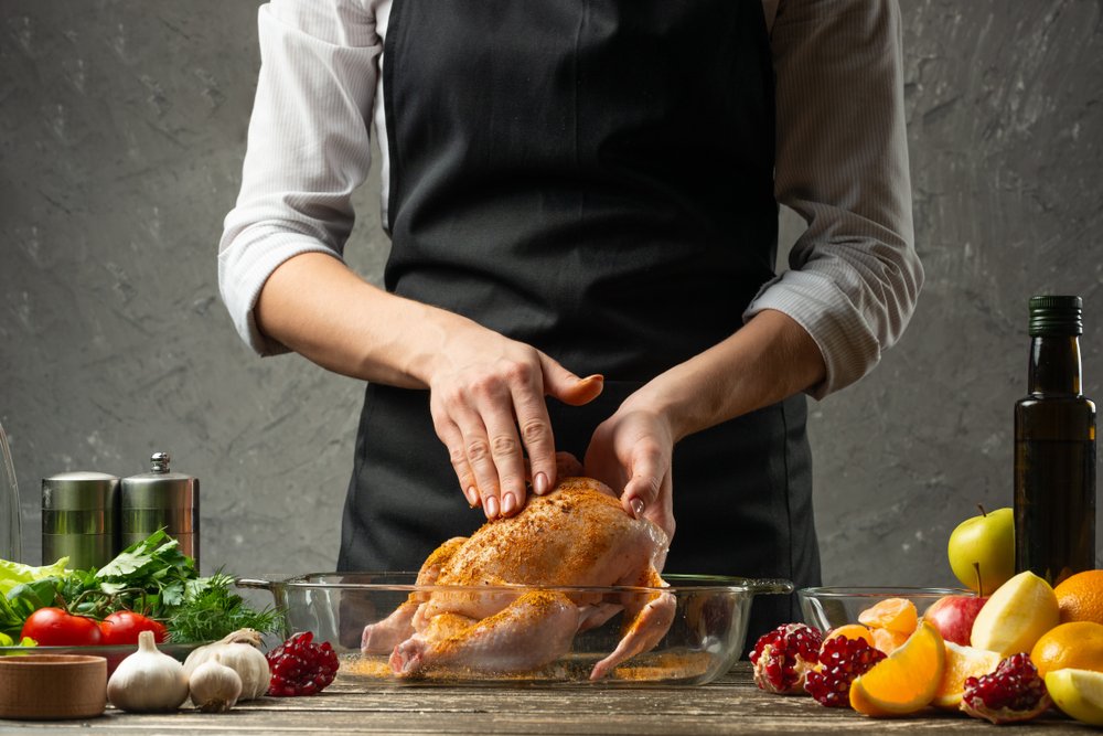 Hombre preparando un pollo entero, rodeado de ingredientes variados. | Foto: Shutterstock