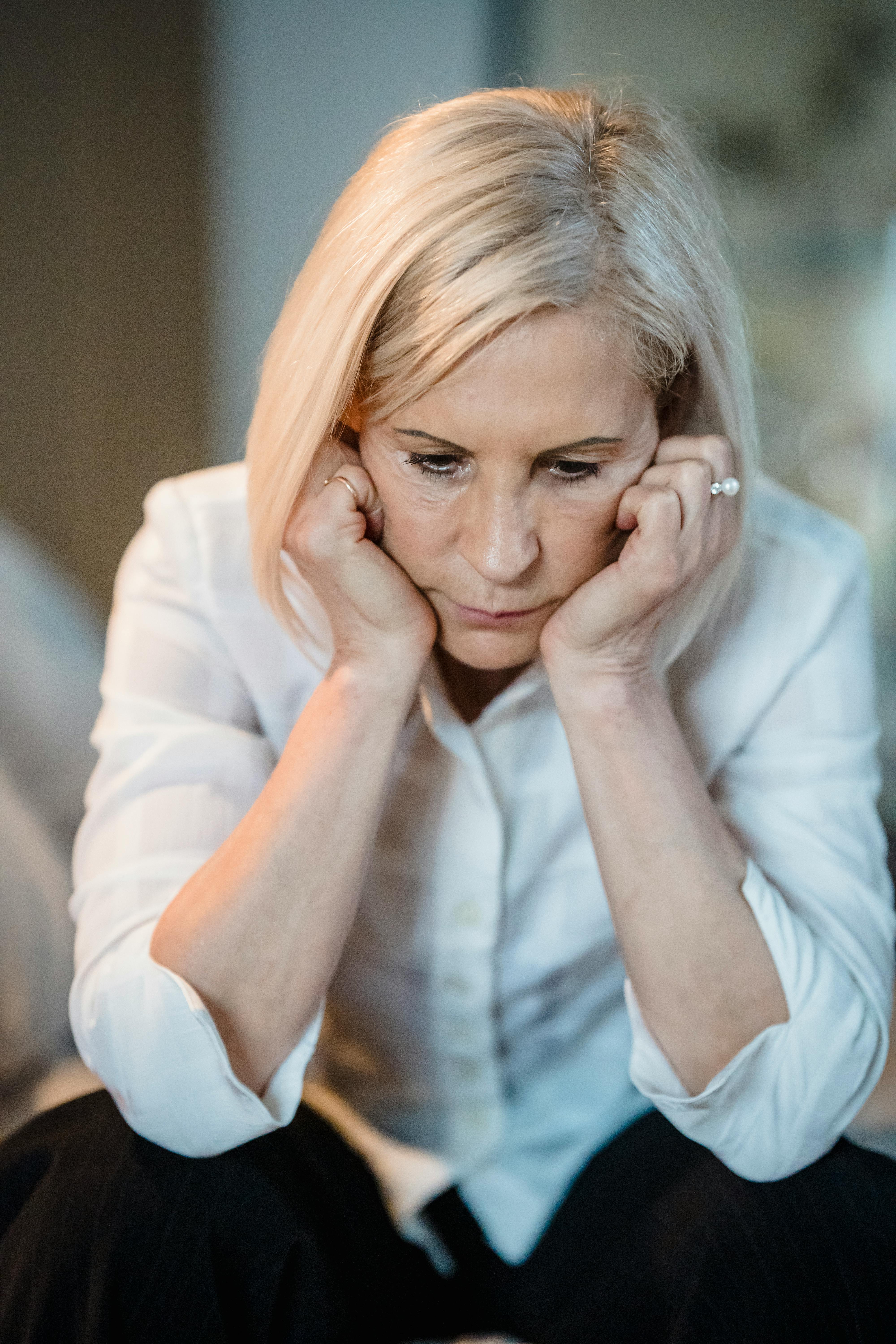 An upset older woman sitting looking down with her hands on her cheeks | Source: Pexels