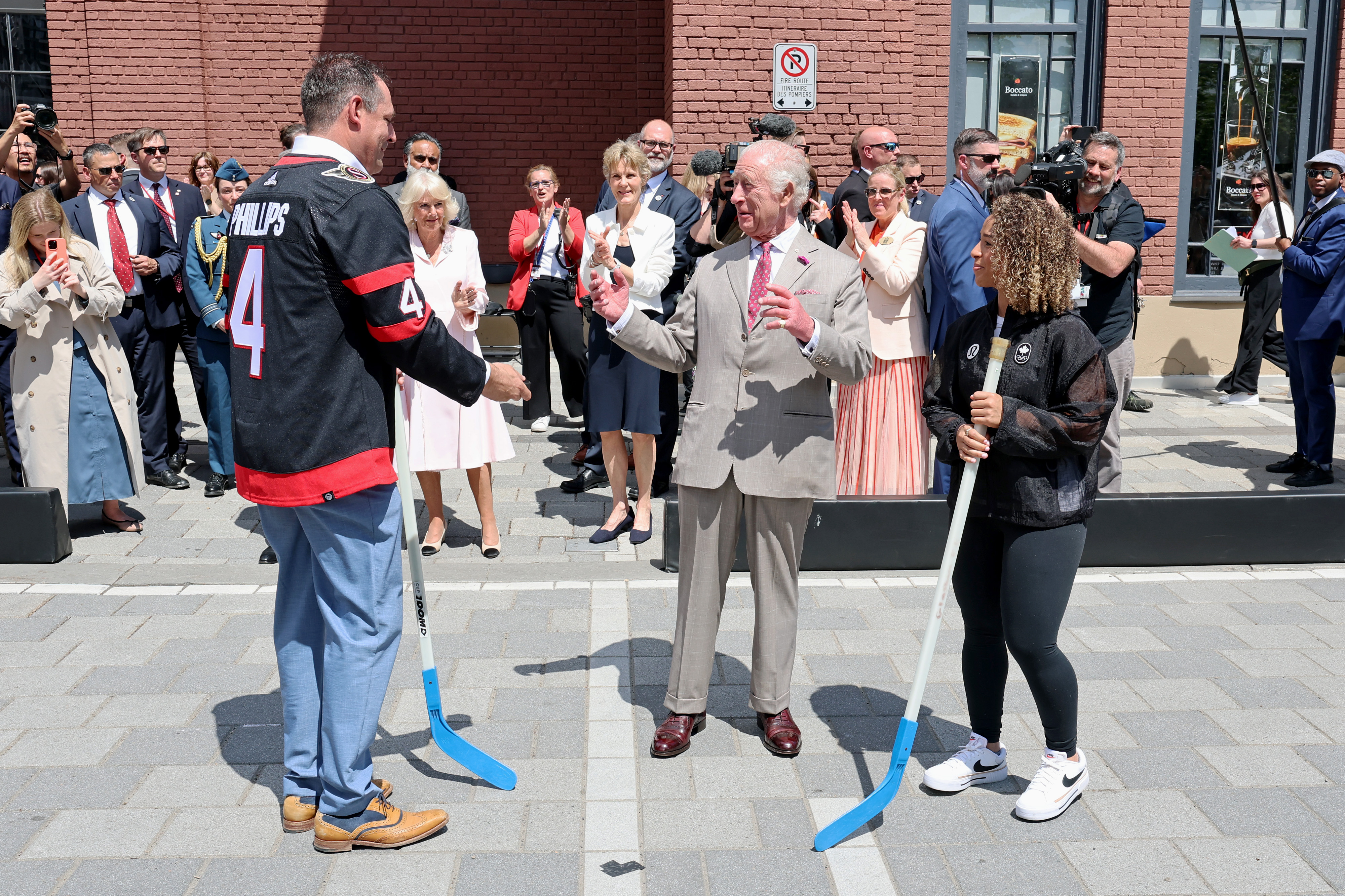 Meanwhile, at the same event in Lansdowne Park, King Charles III drops the puck to officially launch a hockey match featuring former Ottawa Senators player Chris Phillips and Olympic soccer gold medalist Desiree Scott, as Queen Camilla looks on, clapping with a smile.