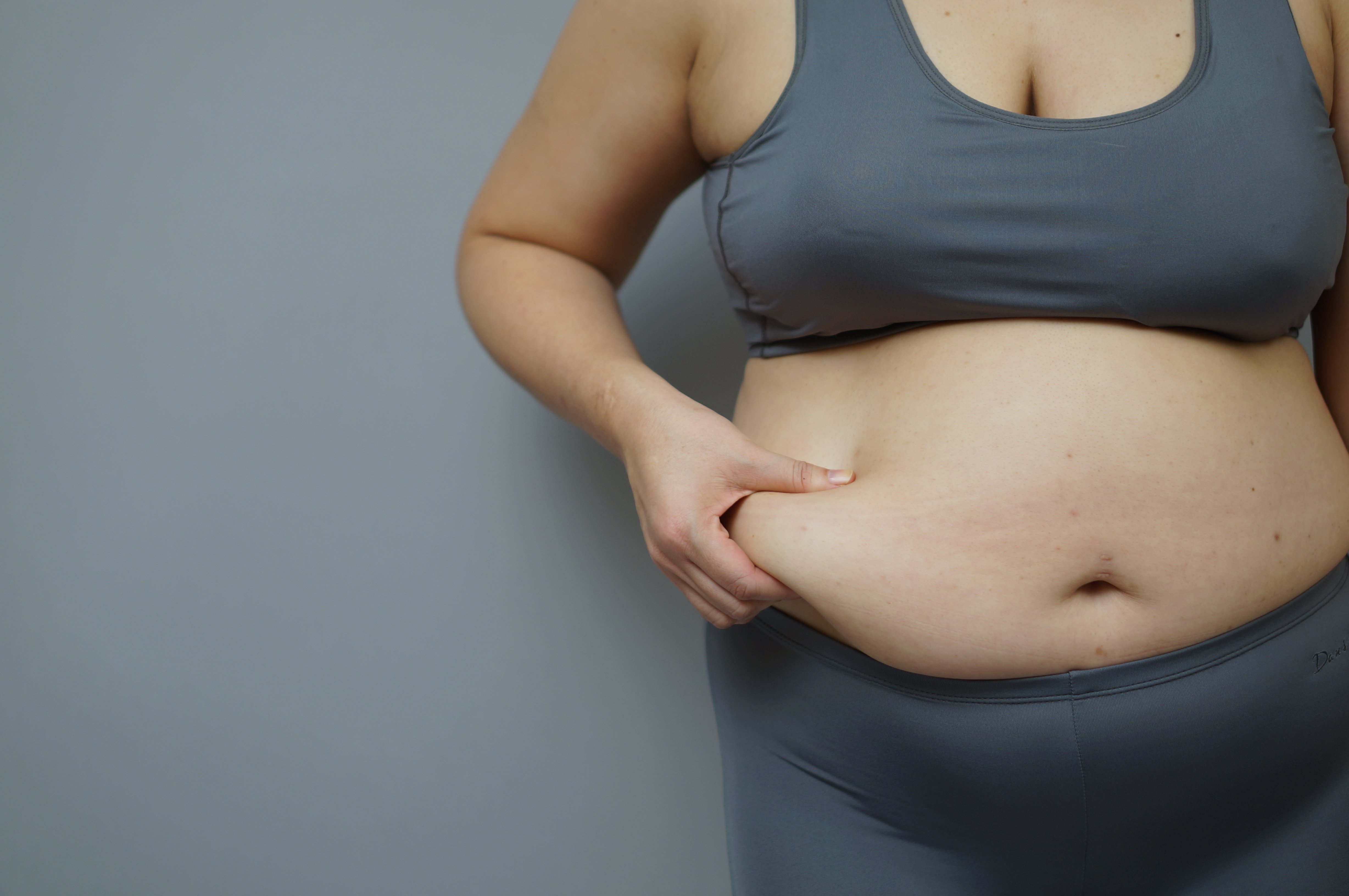 Woman pinching her tummy roll. | Photo: Shutterstock