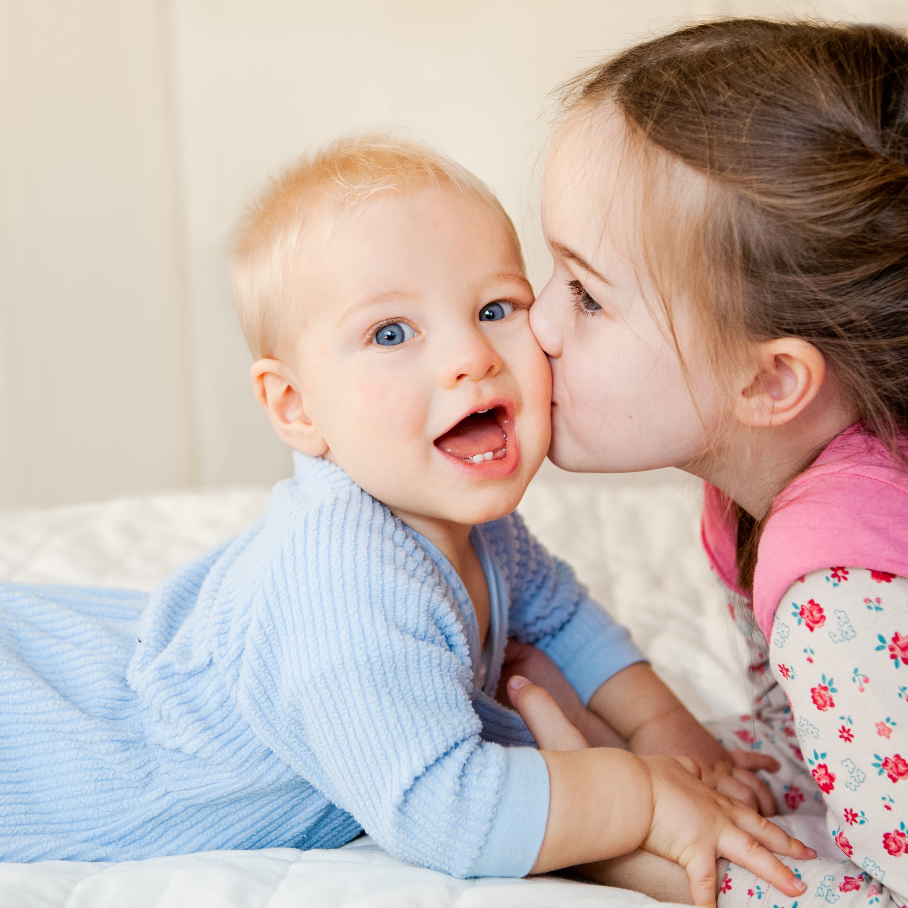 A sister kissing her little brother on the cheek. │Source: Shutterstock