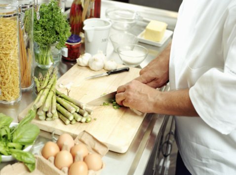 Un chef cuisinier coupe des légumes sur une planche à découper en bois. | Photo : Getty Images