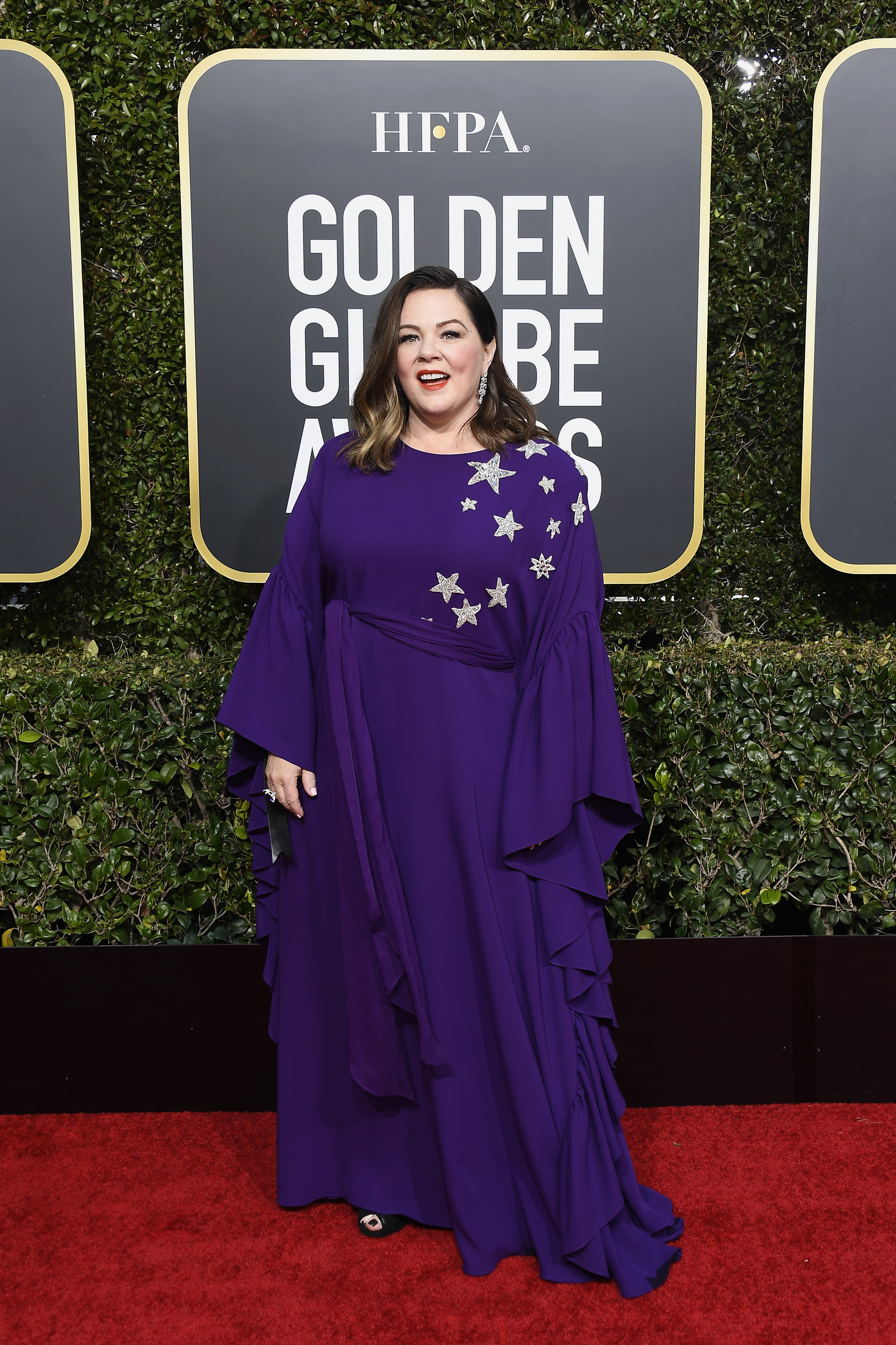 At the 76th Golden Globe Awards, McCarthy embraced softer movement and detail, stepping out in a flowing purple gown with star embellishments that added a more playful, refined touch.