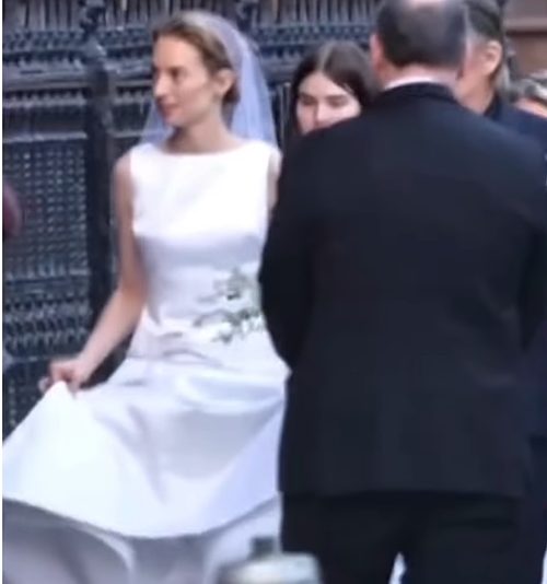 Maya Hawke steps carefully outside the church in a sleeveless white gown and veil, lifting her skirt slightly as she moves. | Source: Instagram/relationships.usa