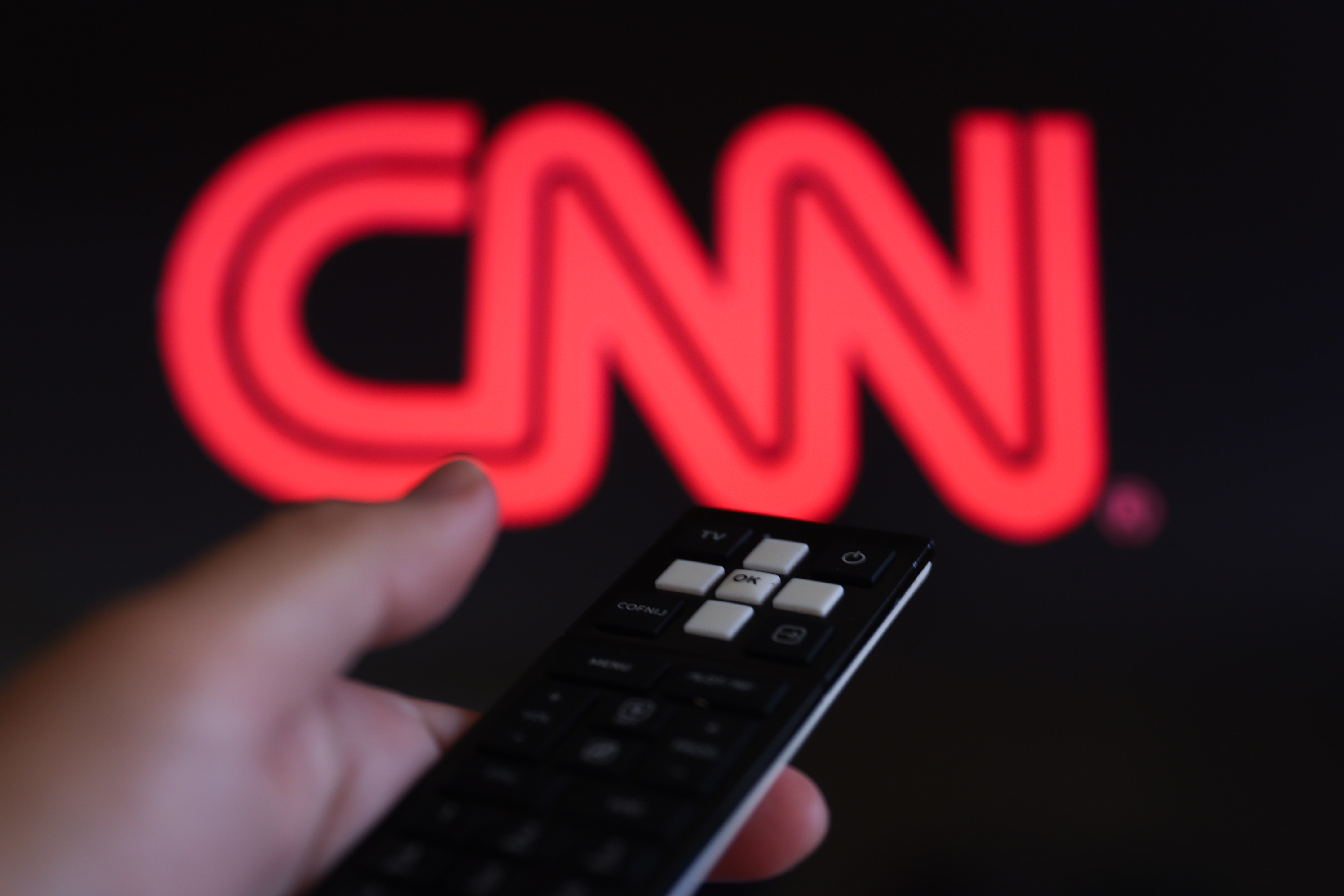 The CNN logo on a TV screen with a person's hand holding a remote in Poland on August 7, 2024. | Source: Getty Images