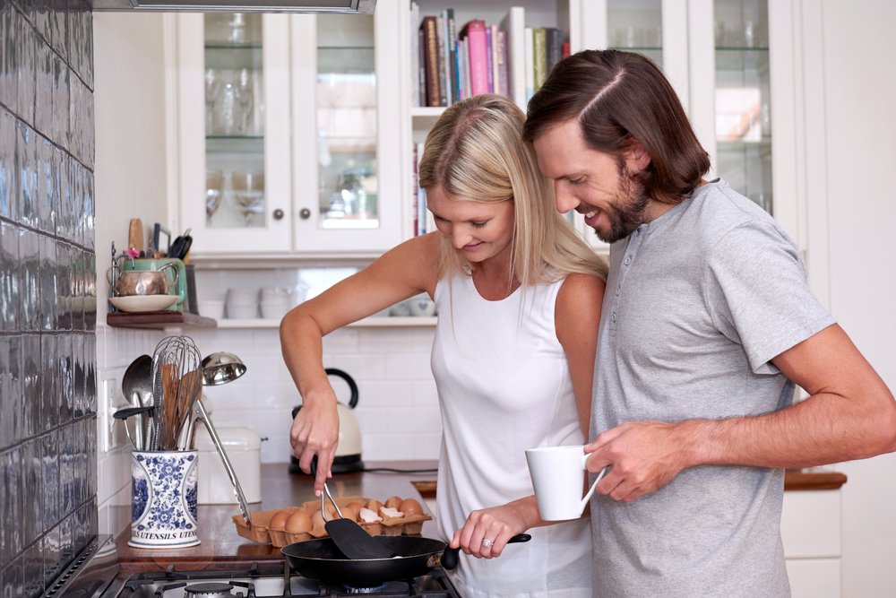 Joven pareja preparando el desayuno de huevos en la estufa en la cocina de casa. I Foto: Shutterstock