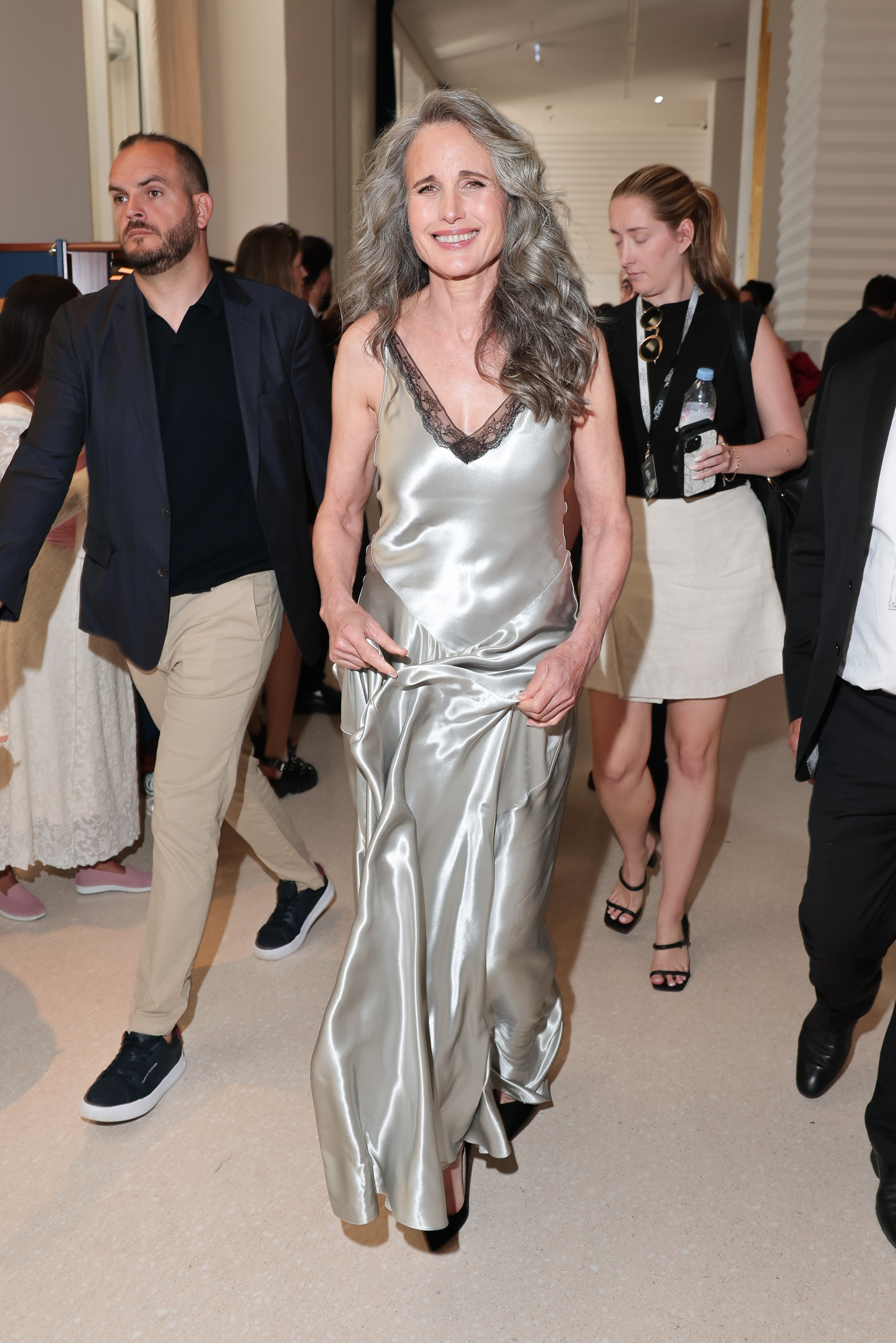 Captured at Hotel Martinez, Andie MacDowell beams while making her way indoors during day three of the 78th Cannes Film Festival. She lifts the hem of her silver gown to navigate through the crowd.