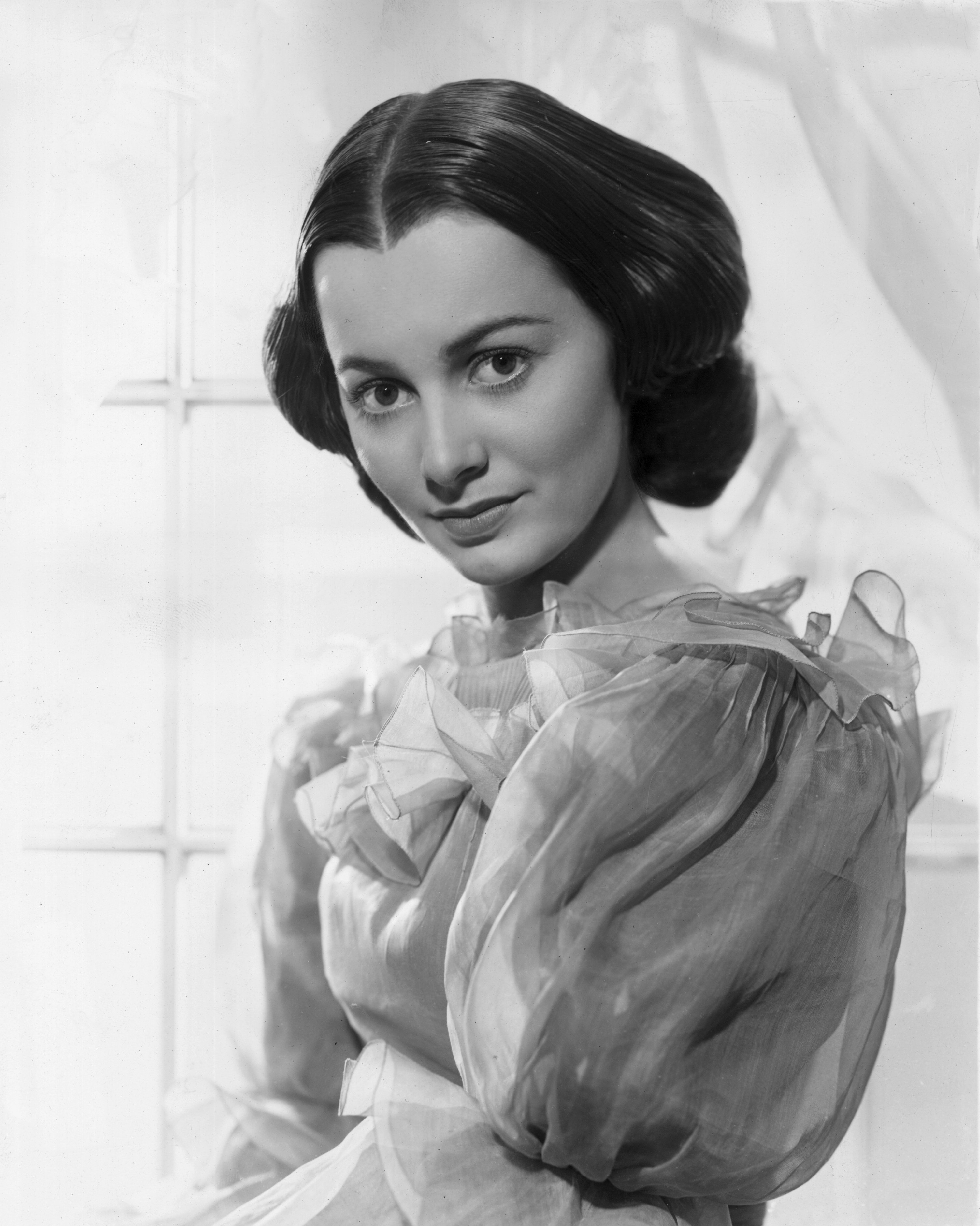 circa 1939: Promotional studio portrait of American actor Olivia de Havilland, standing in front of a window in a promotional portrait for 'Gone With The Wind'. She wears a gown, with her hair parted and pulled back. | Source: Getty Images