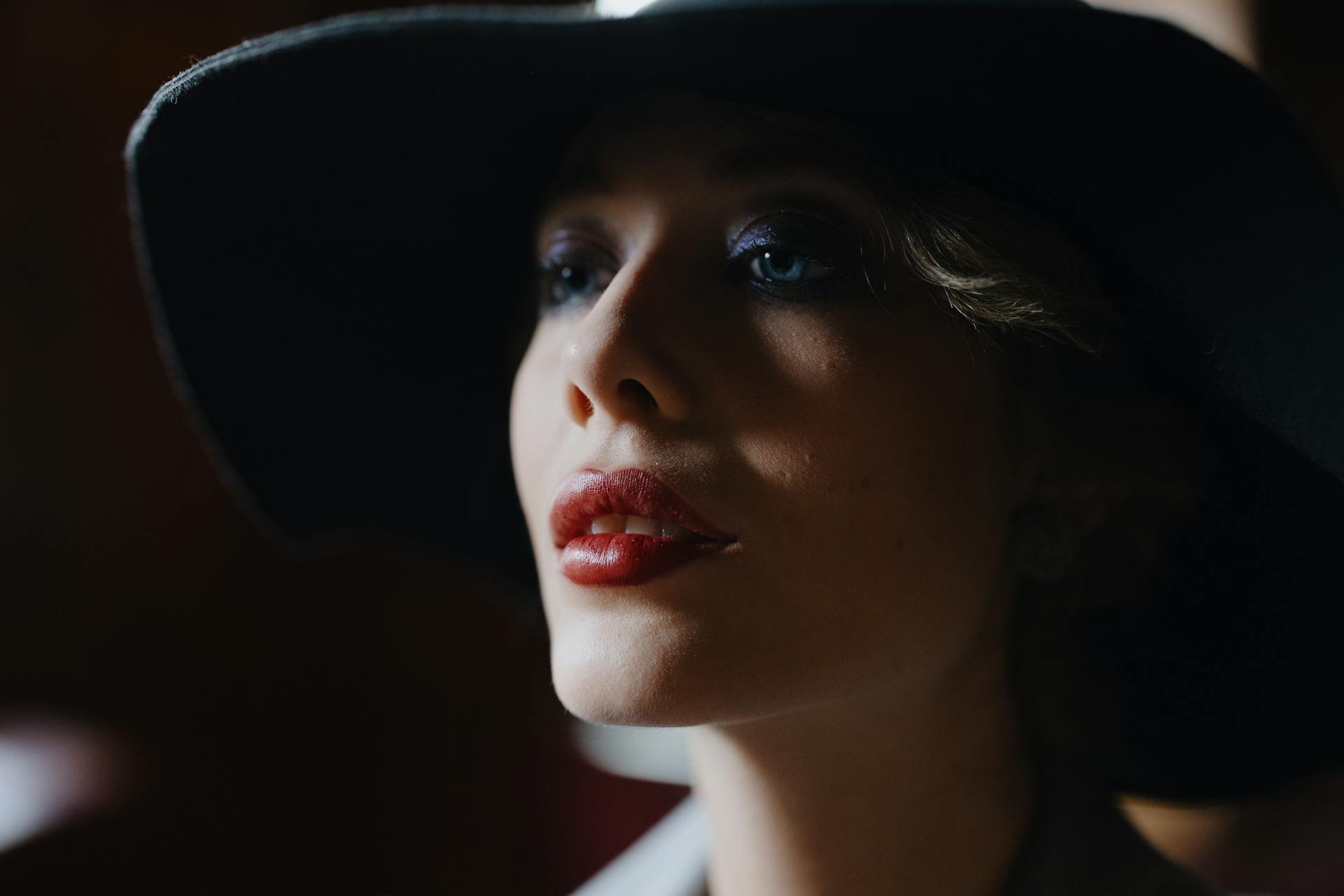 Una hermosa mujer con lápiz labial rojo y sombrero negro mira hacia un lado | Fuente: Pexels