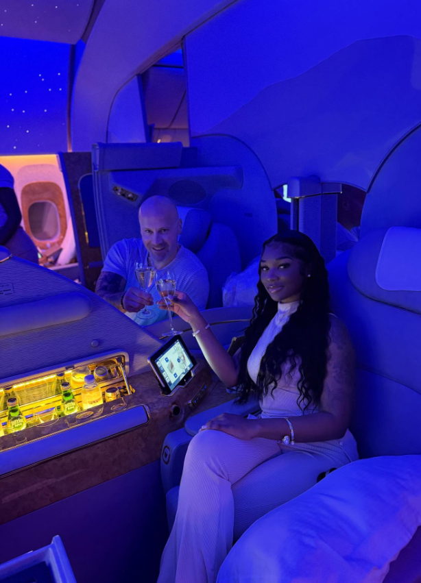 Under soft blue cabin lights, Ashly Robinson and Joe McCann raise their glasses in quiet celebration, turning a private flight into a moment of effortless luxury. | Source: Instagram/ashleejenae