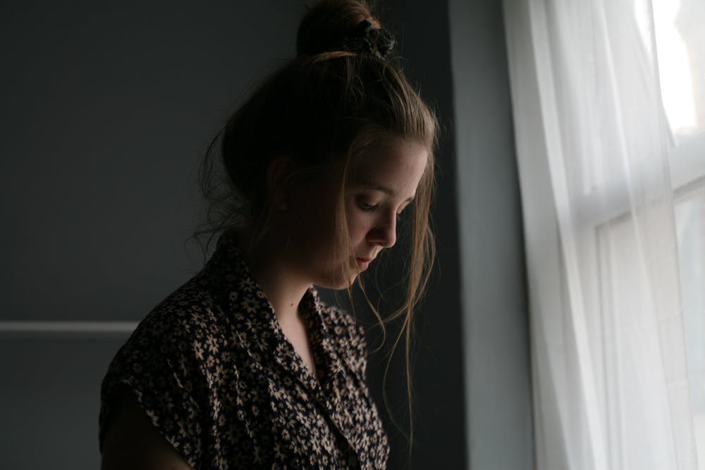 An unhappy woman standing beside the window. | Photo: Pexels