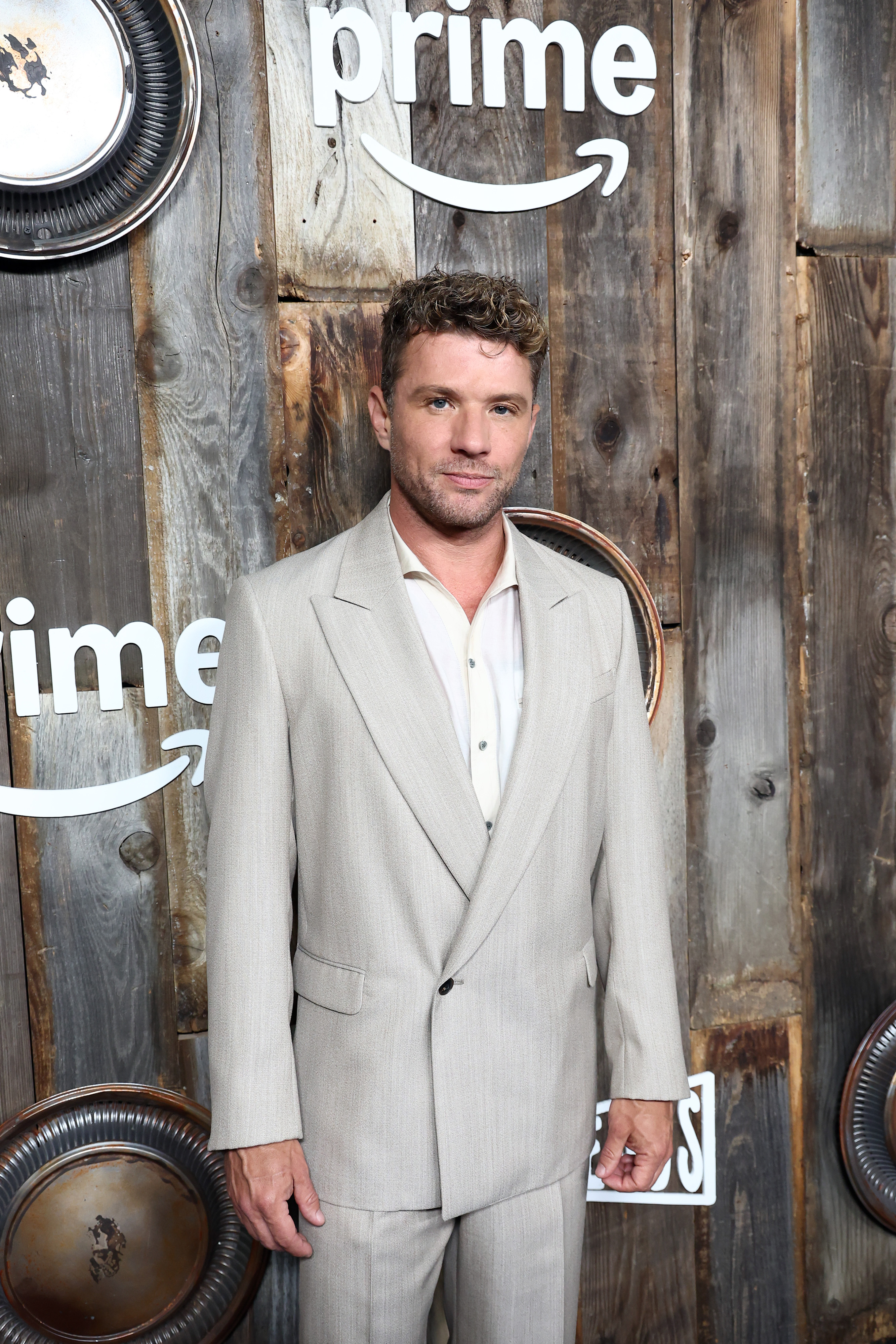Standing before Prime Video's signature step-and-repeat wall, Ryan Phillippe attends the "Motorheads" screening at the Academy Museum, confidently dressed in a relaxed light suit ensemble, with a clean shave and tousled curls completing the look.