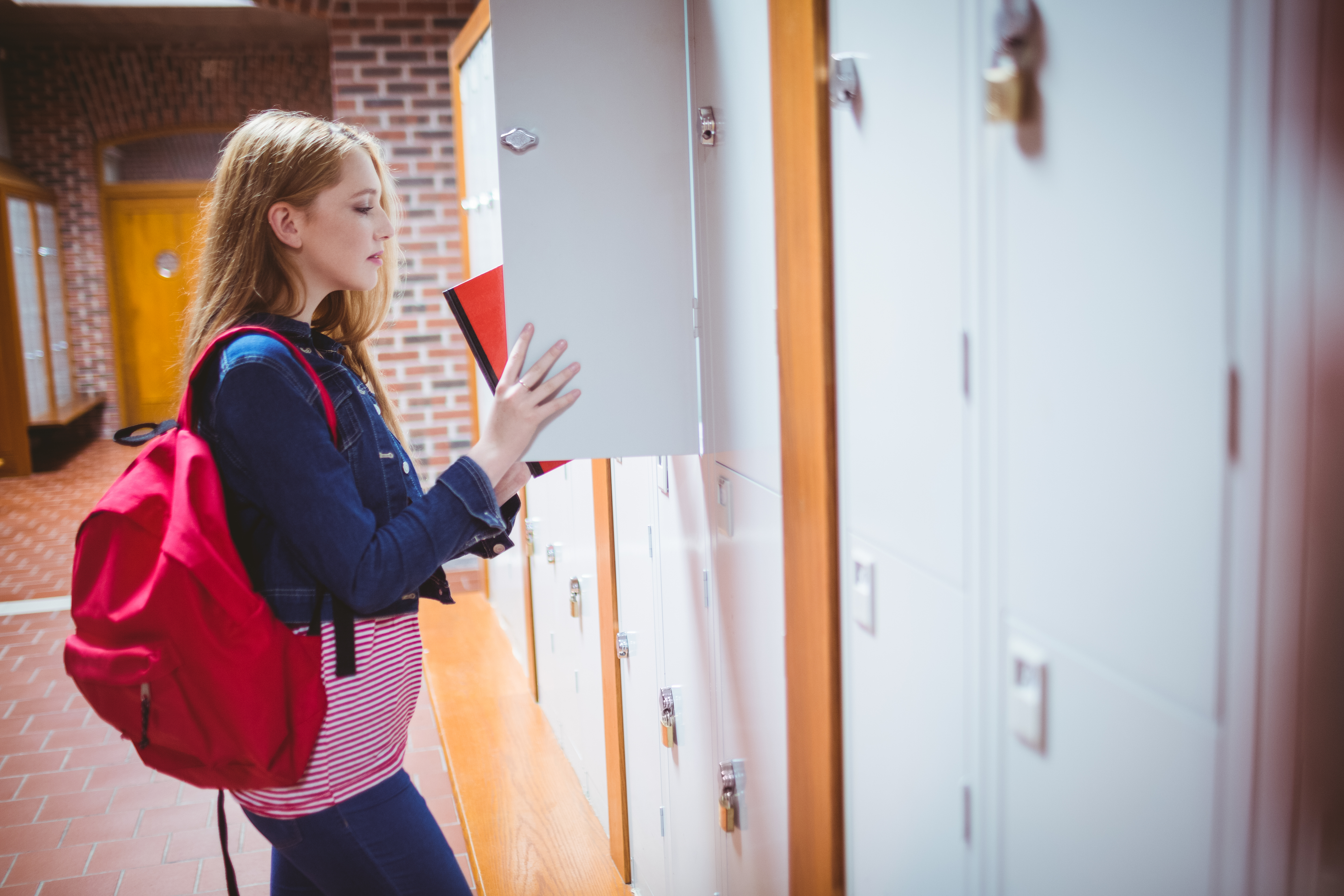 Student with backpack putting notebook in the locker at school. | Source: Shutterstock