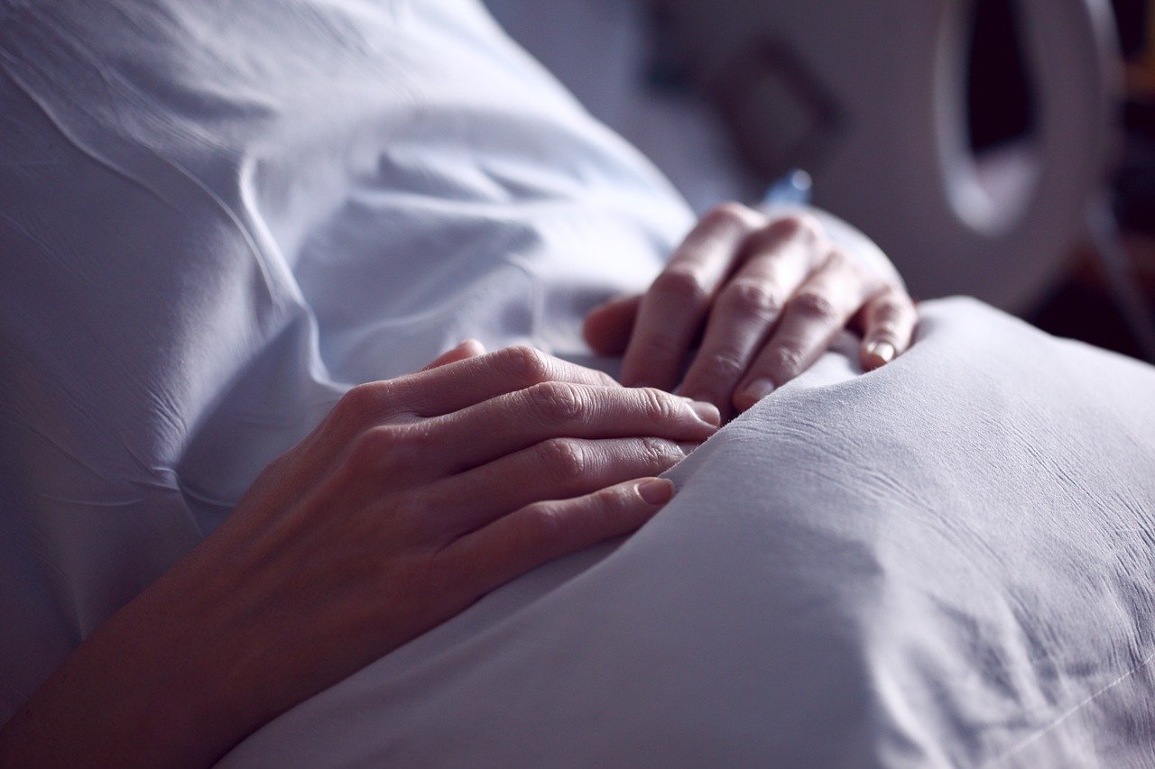Eine Frau, die sich an ihren Bauch fasst, während sie in einem Krankenhausbett liegt | Quelle: Pixabay/Sharon McCutcheon