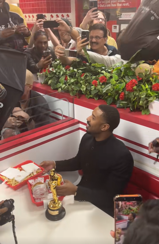 Michael B. Jordan smiles while holding his Oscar inside an In-N-Out Burger booth beside a tray of burgers and fries. | Source: TikTok/donovanfilmz