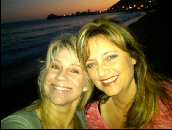 Dina Norris DiCiolli smiles brightly beside a companion during a beachside sunset, the fading light casting a warm glow over the scene. | Source: Facebook/DinaDiCiolli