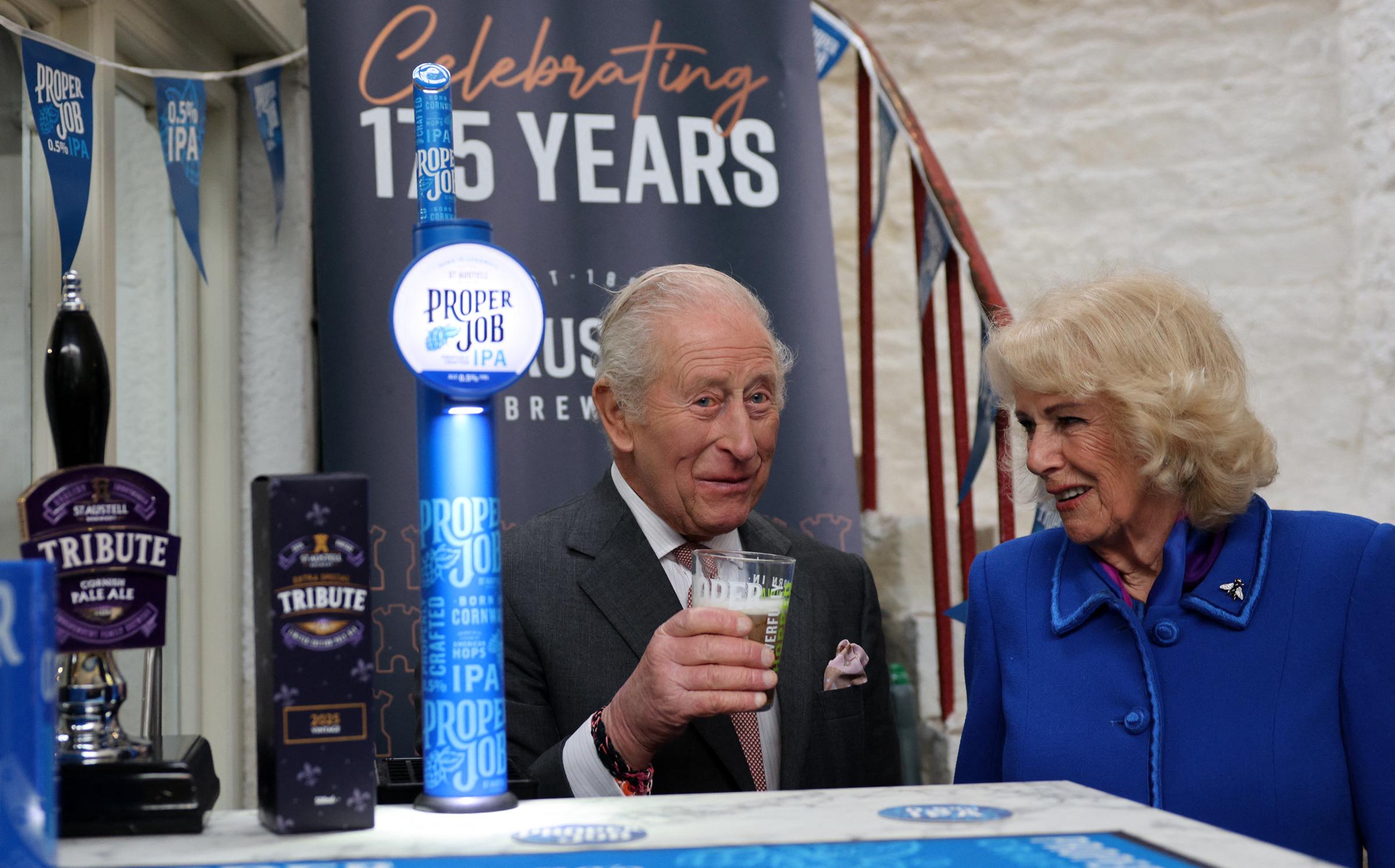Queen Camilla reacts as King Charles III tastes a pint of St Austell Brewery's Proper Job IPA 0.5% that he pulled, during a visit to the The Market Hall on 24 March 2026 in St Austell, England. | Source: Getty Images