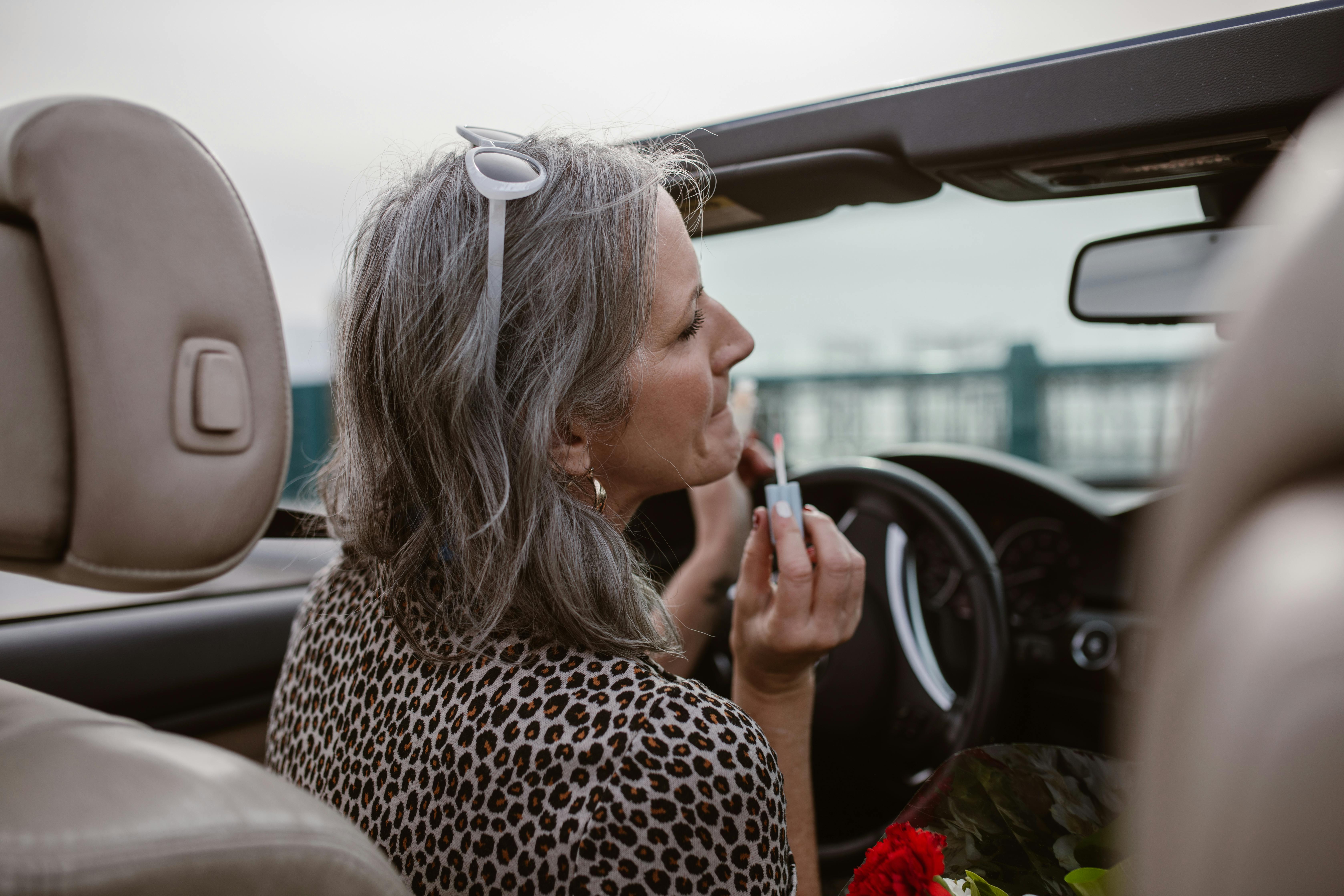 A woman applying lip balm using her car's rear mirror | Source: Pexels