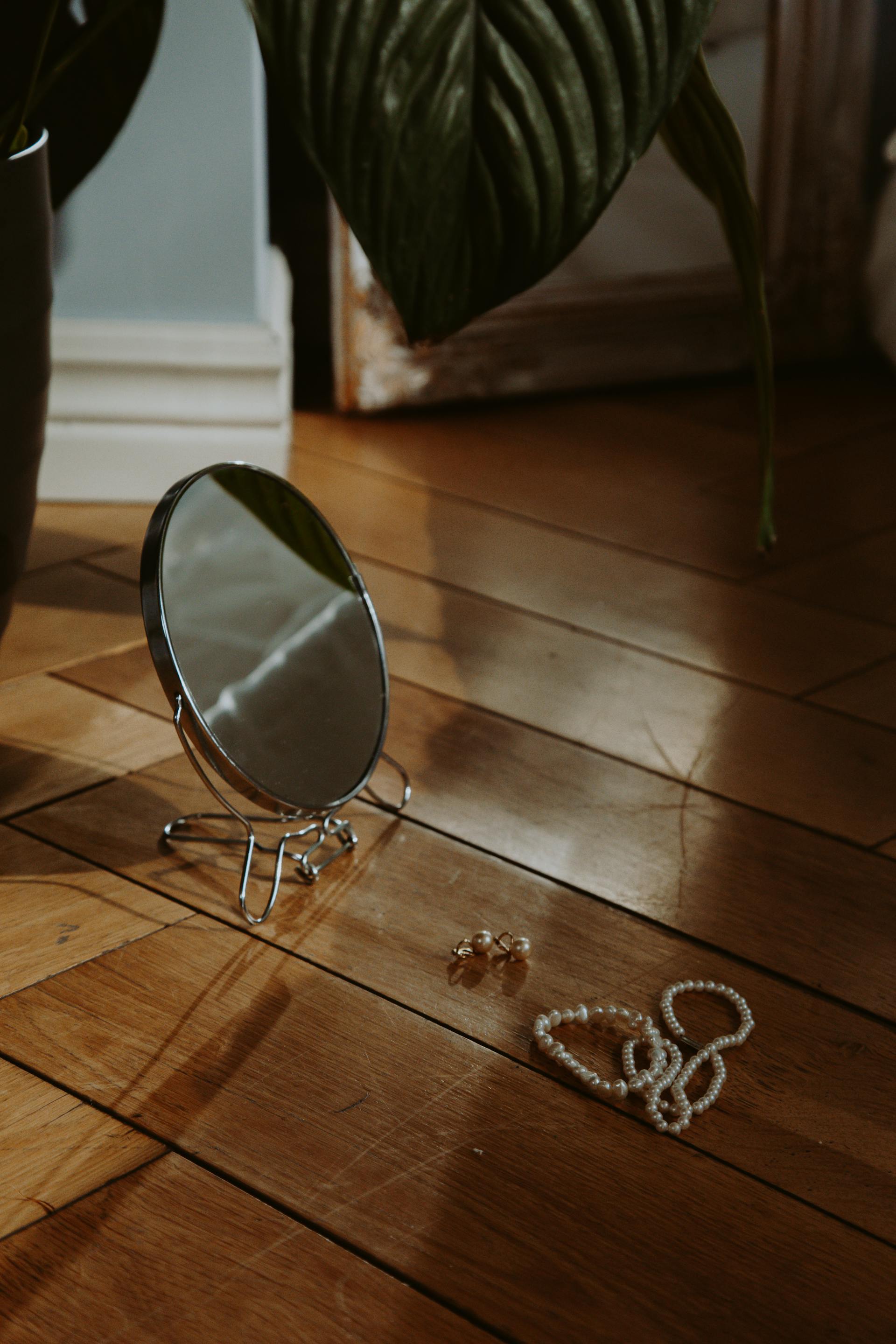 A sliver-framed round mirror and jewelry items lying on the wooden floor | Source: Pexels