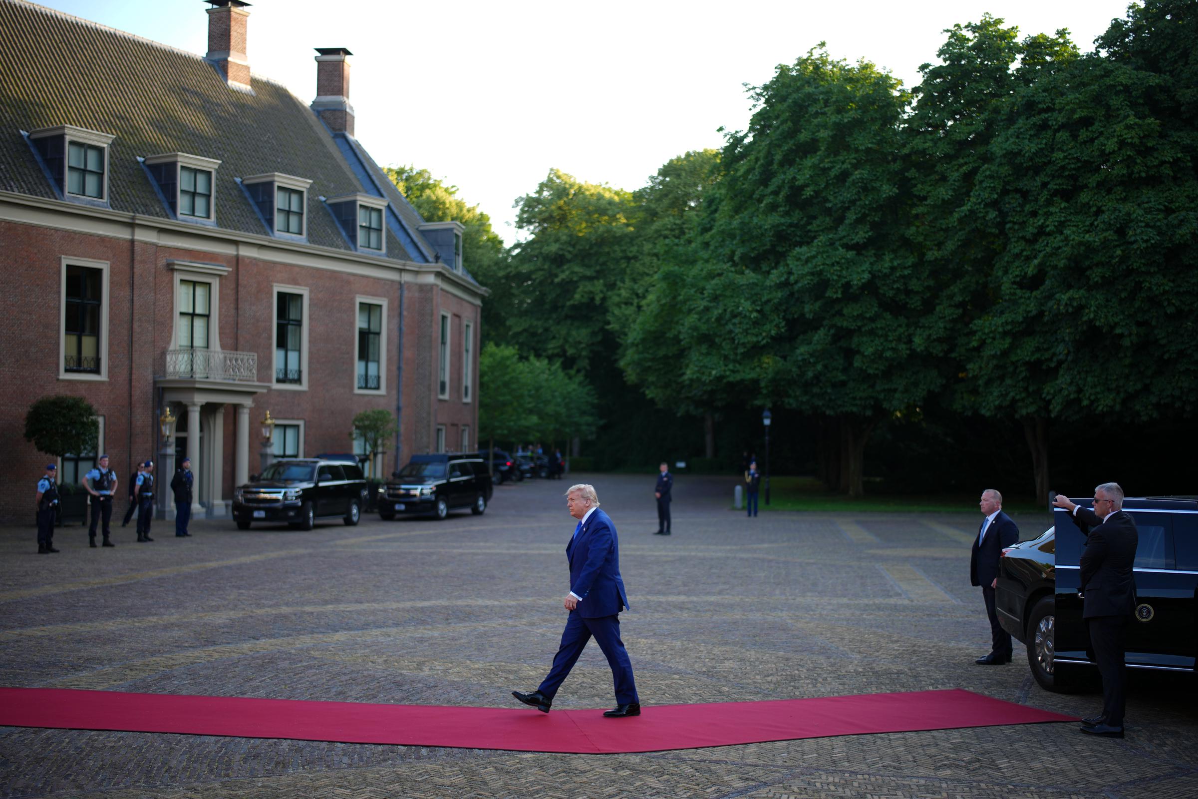 Trump walks along a red carpet toward Huis ten Bosch Palace in The Hague, with bodyguards standing near his car, as he arrives for a dinner hosted by the King and Queen of the Netherlands that is attended by other NATO leaders and their spouses.