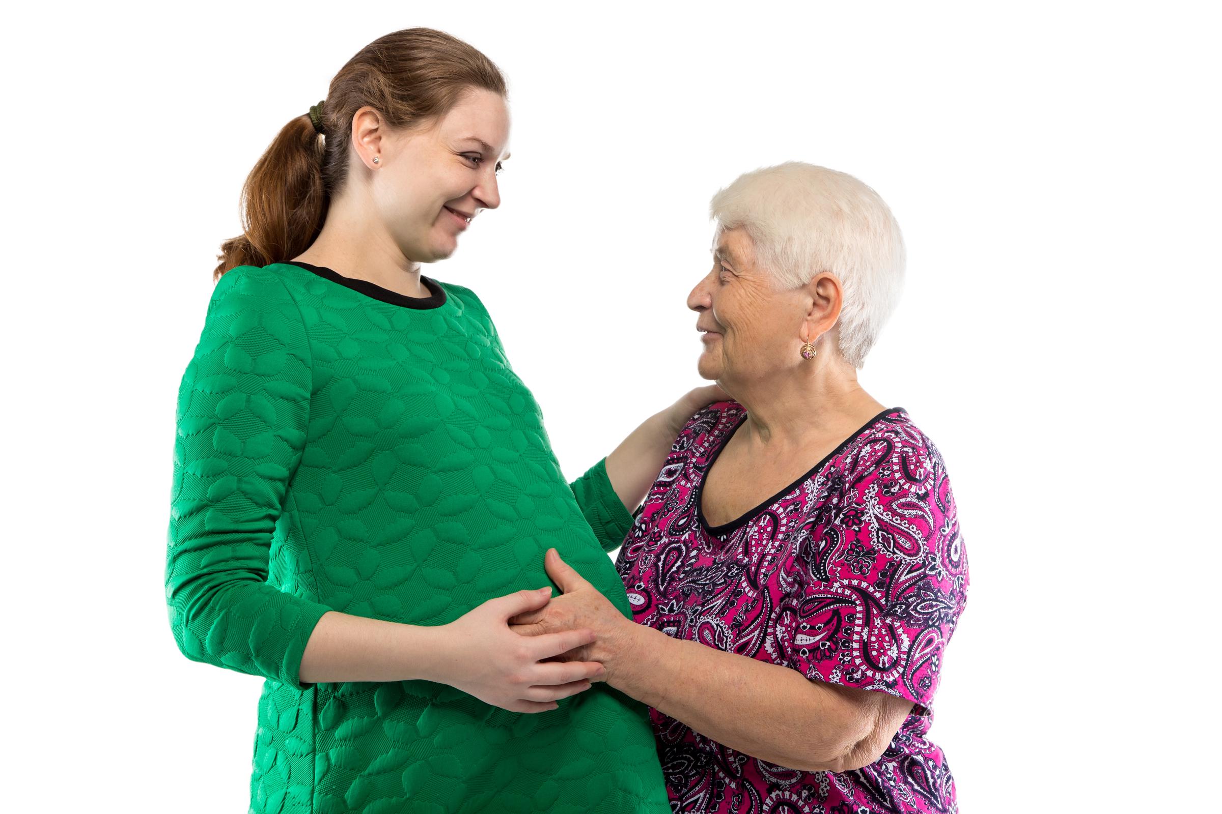 Older woman smiling at a pregnant woman while cradling her belly | Source: Shutterstsock