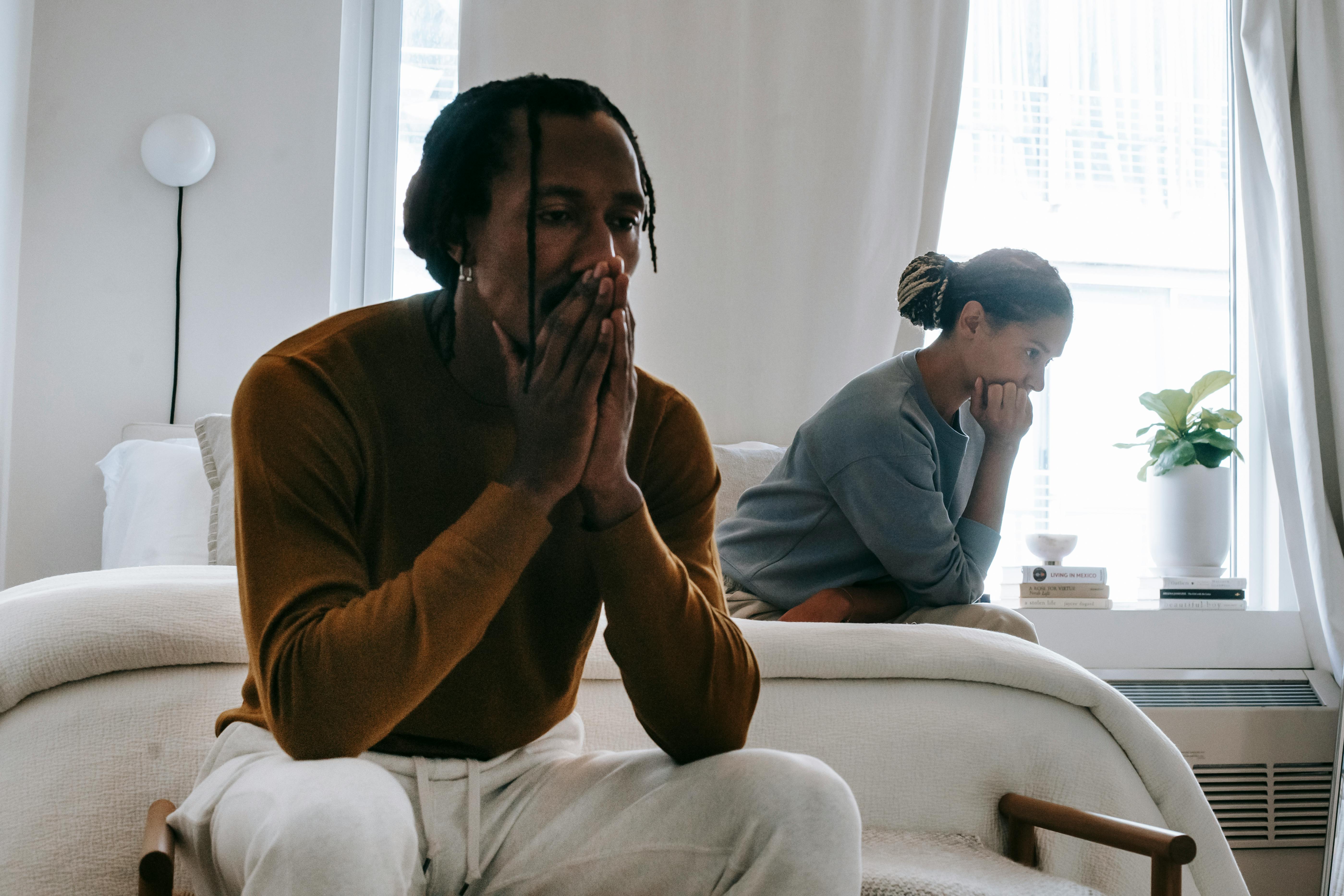 A distressed couple sitting on different ends in their bedroom | Source: Pexels