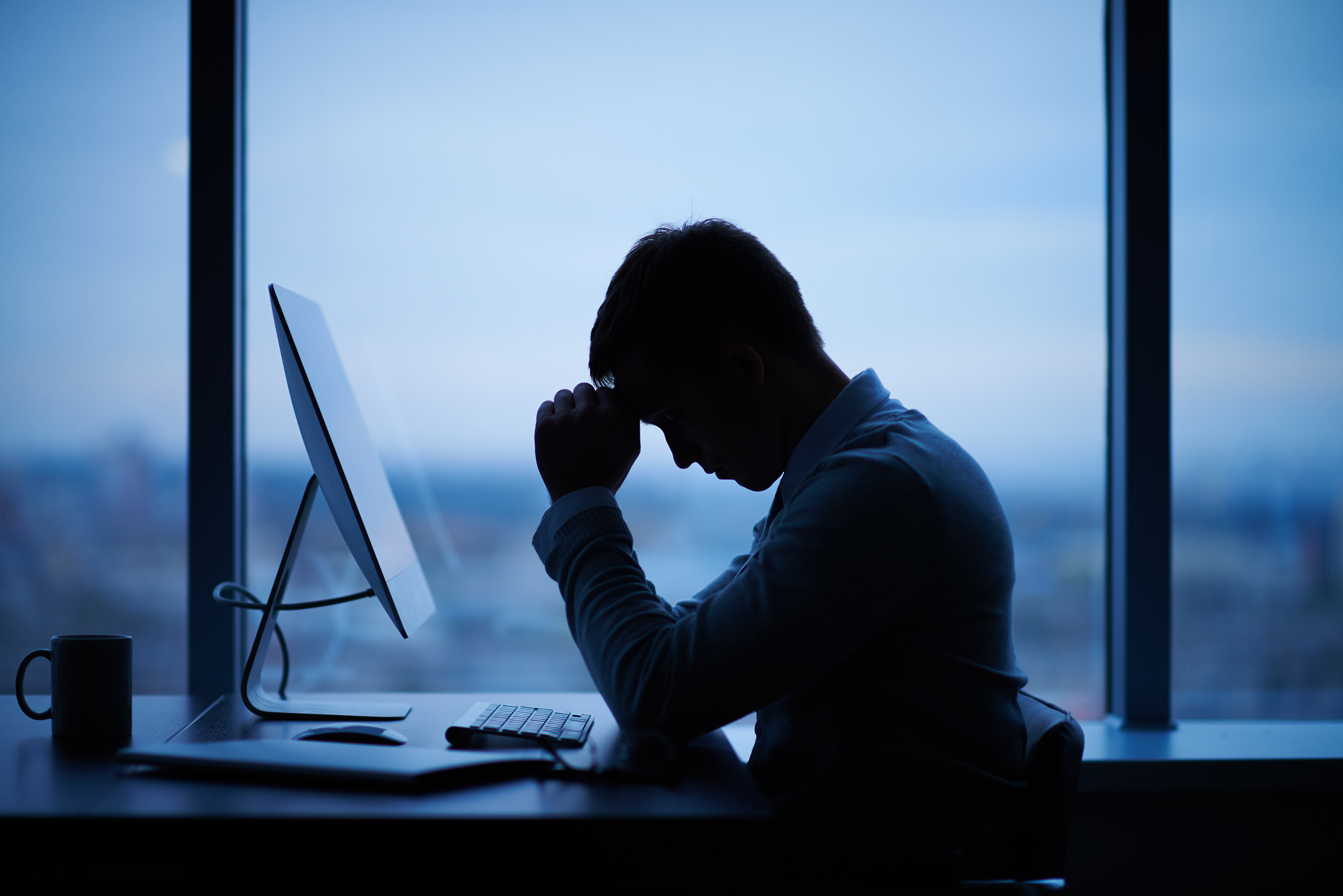 Tired man sitting in front of a computer in office | Source: Shutterstock