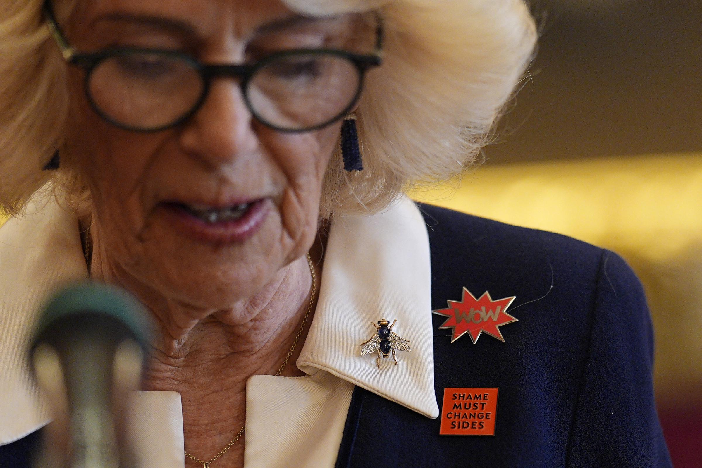 Queen Camilla's lapel badges read "WoW" and "Shame Must Change Sides" as she delivers her speech at St James's Palace on 10 March 2026 in London, England. | Source: Getty Images