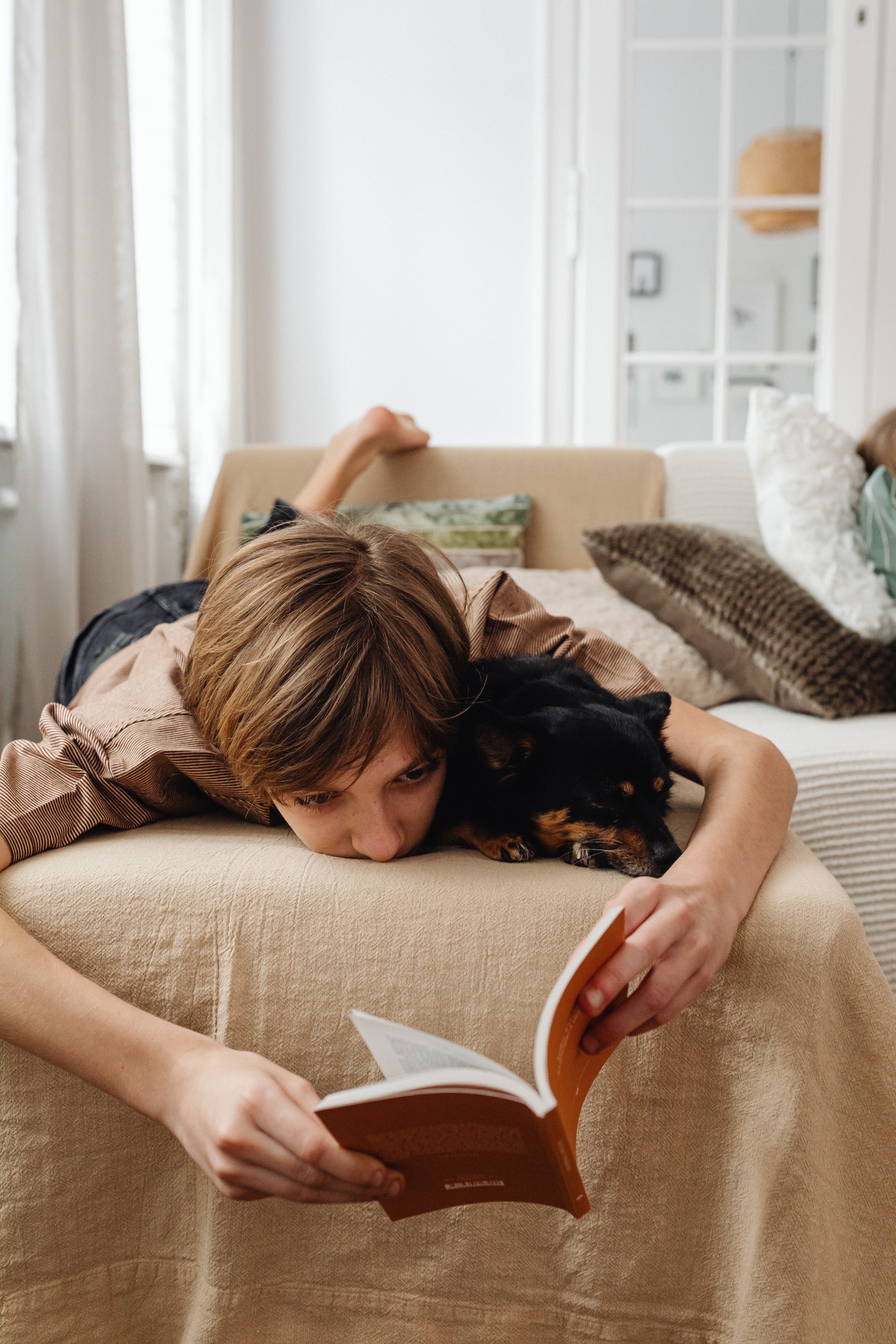 A little boy reading a book with his dog while lying on his bed | Source: Pexels