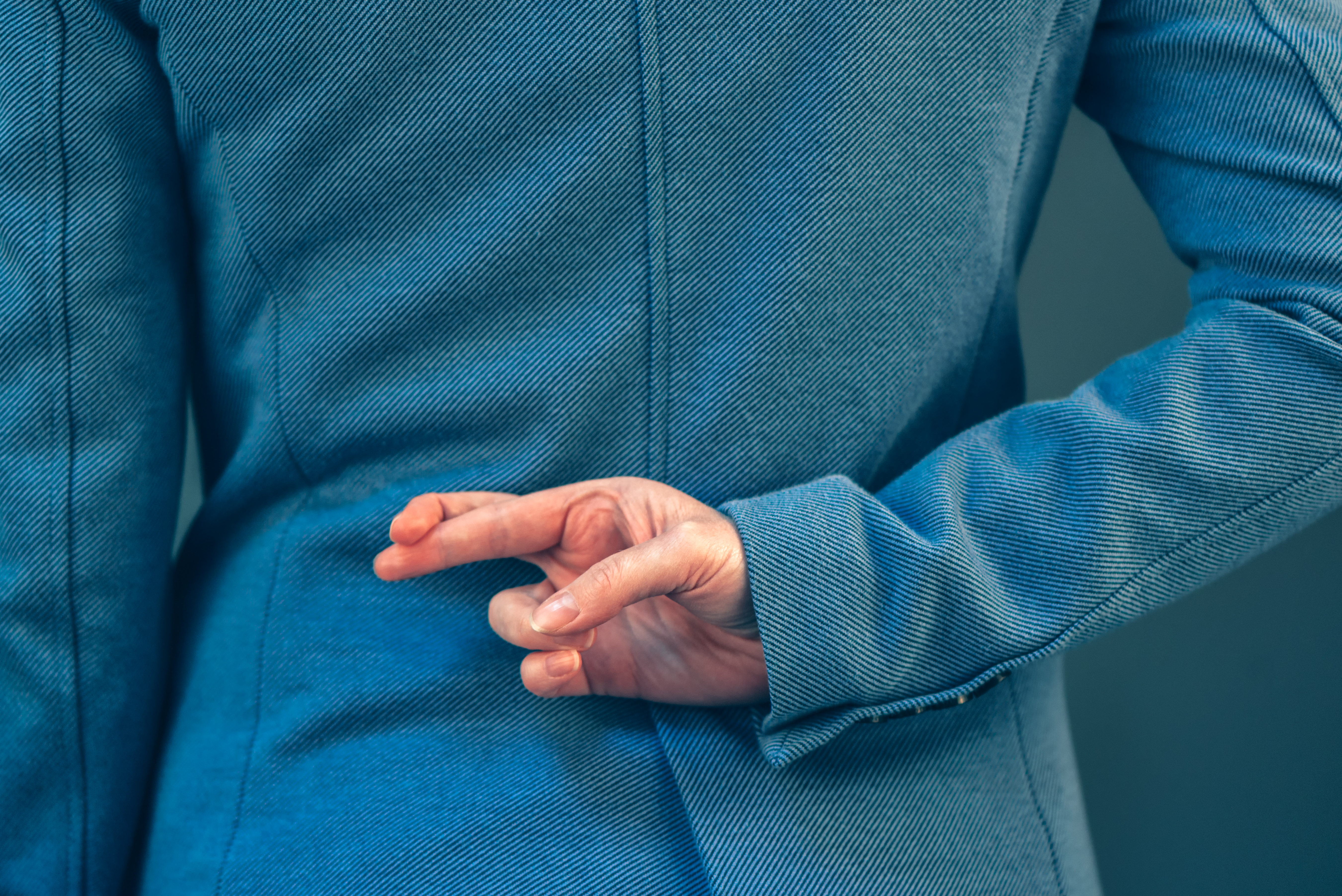 A man secretively crossing his fingers behind his back. | Source: Getty Images