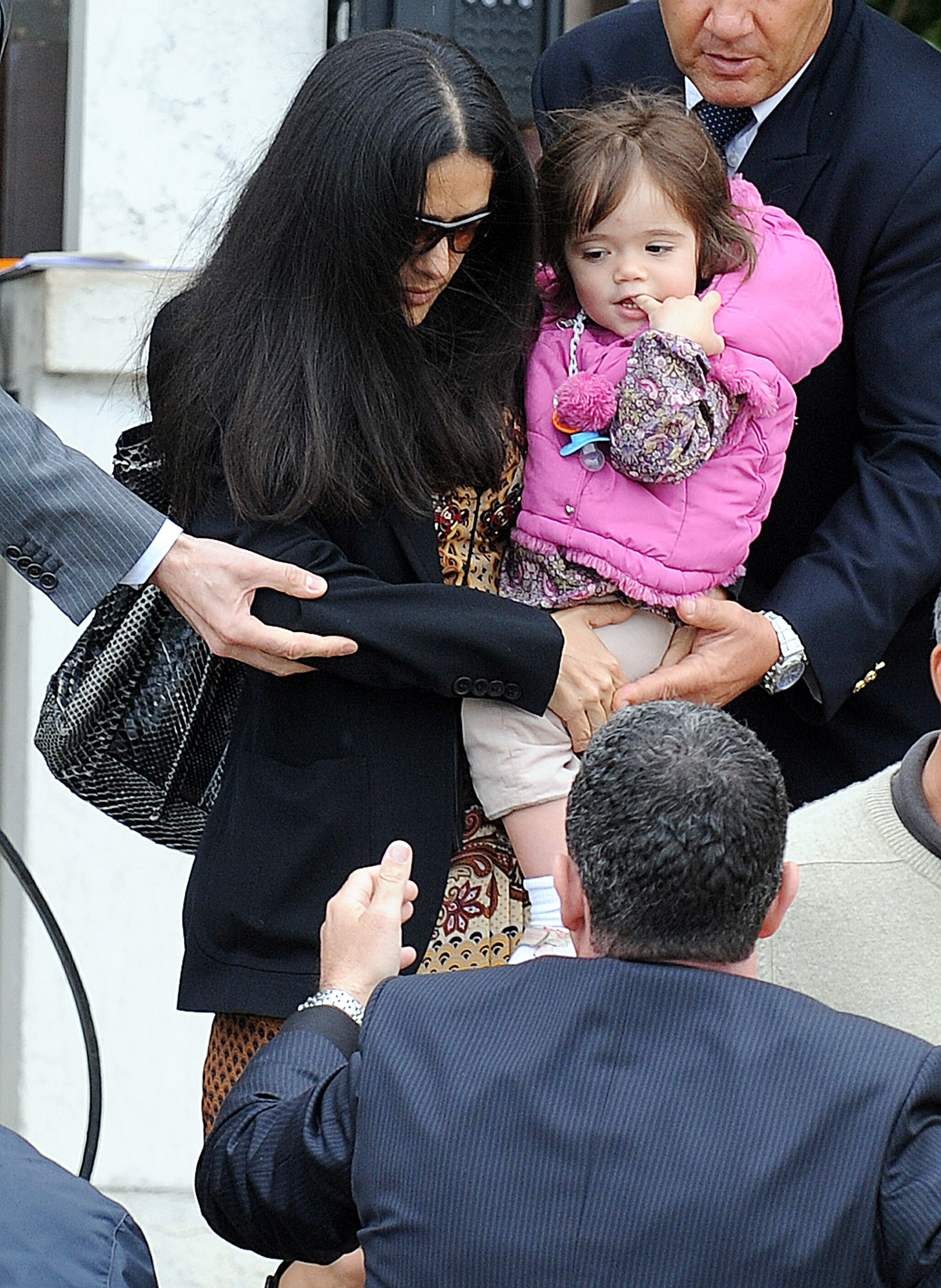 Navigating a crowd outside Venice's Cipriani Hotel, Salma Hayek holds Valentina Pinault in her arms as security personnel assist them through. Wearing oversized sunglasses and a black coat layered over a patterned dress, the actress maintains a low profile. Valentina, bundled in a vibrant pink puffer jacket and floral-print top, clings to her mother.