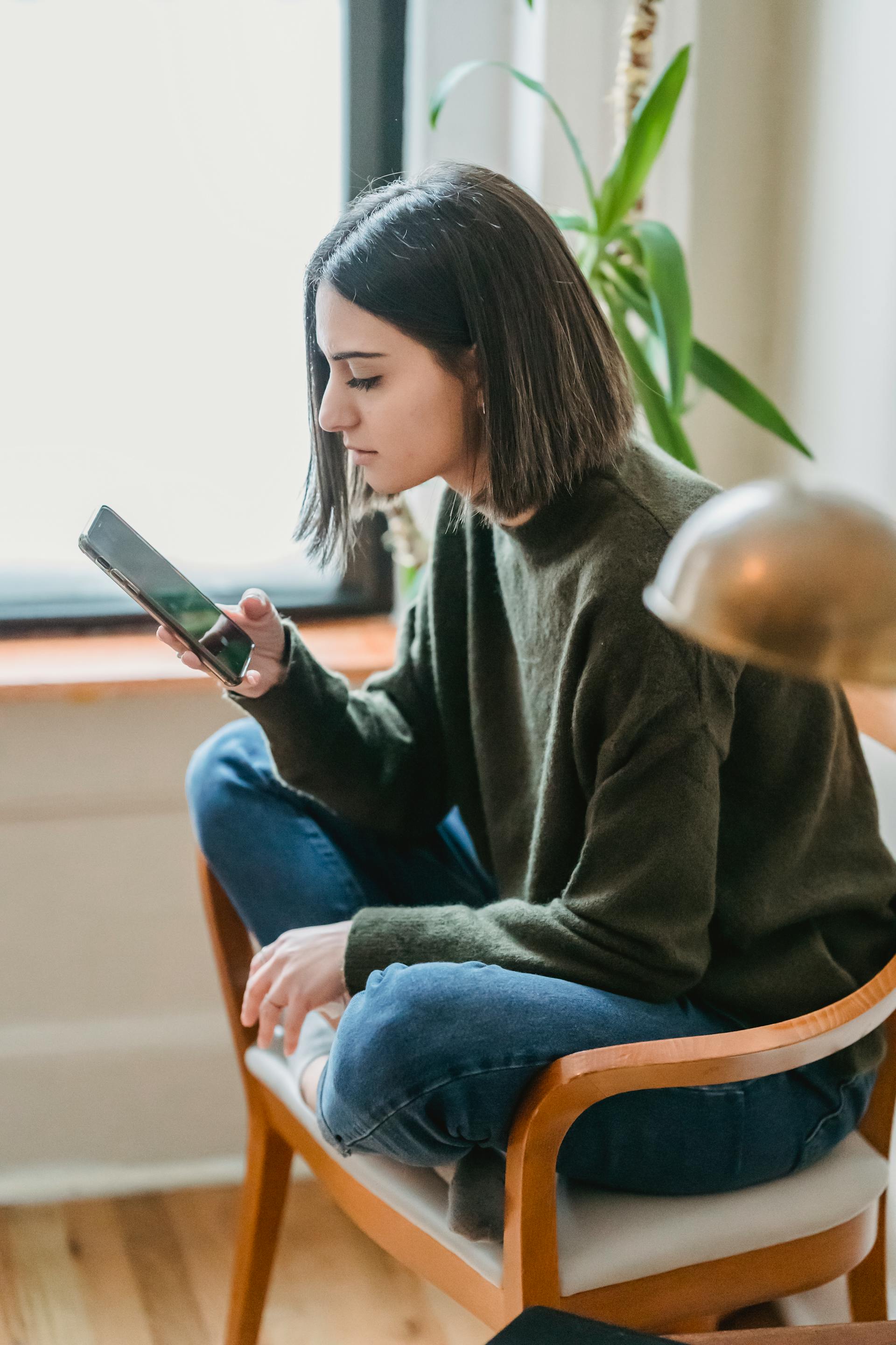 A woman sitting on a chair and looking at her phone | Source: Pexels