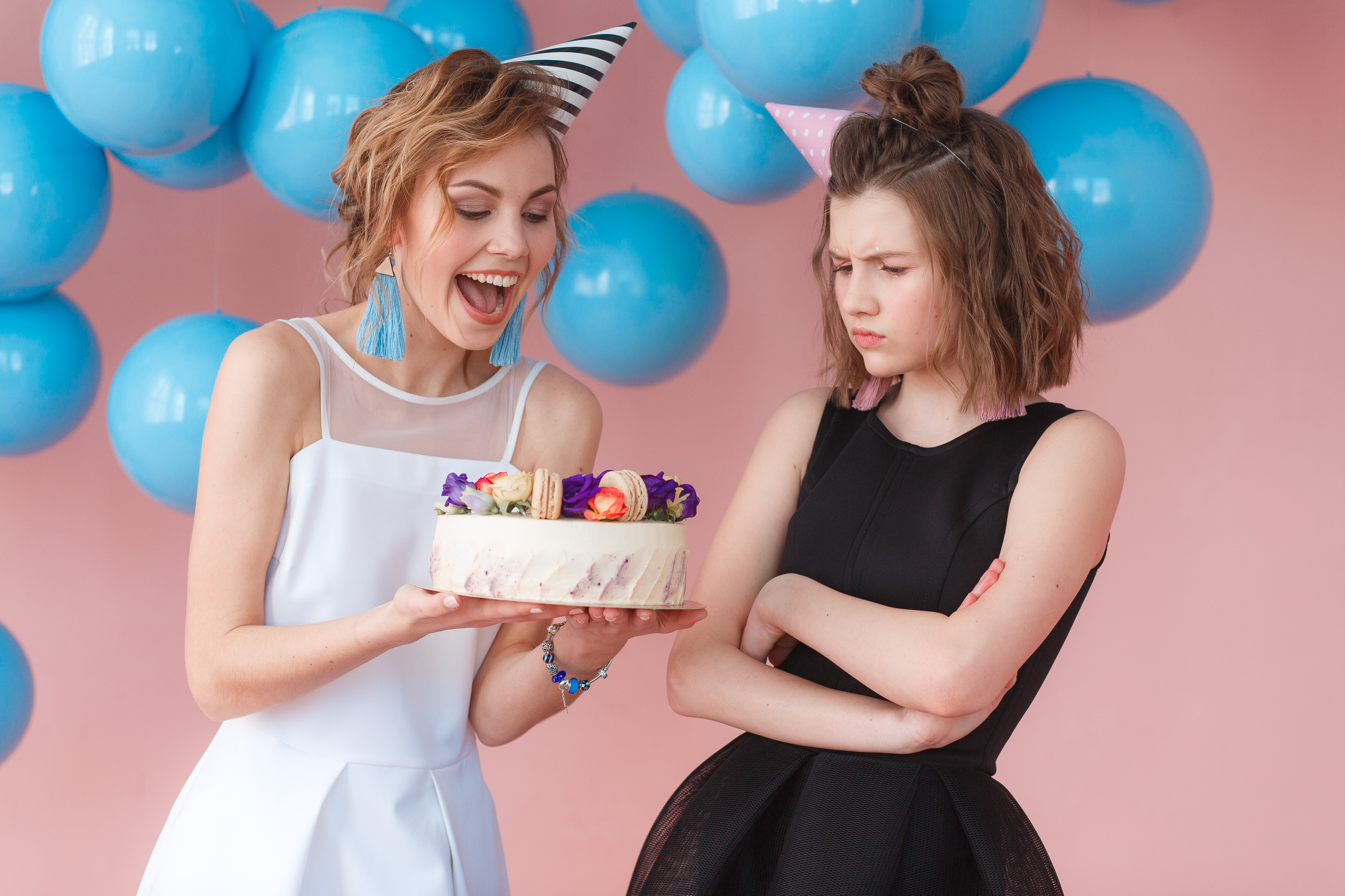 Two teenagers holding a birthday cake, one smiling and the other frowning | Source: Freepik