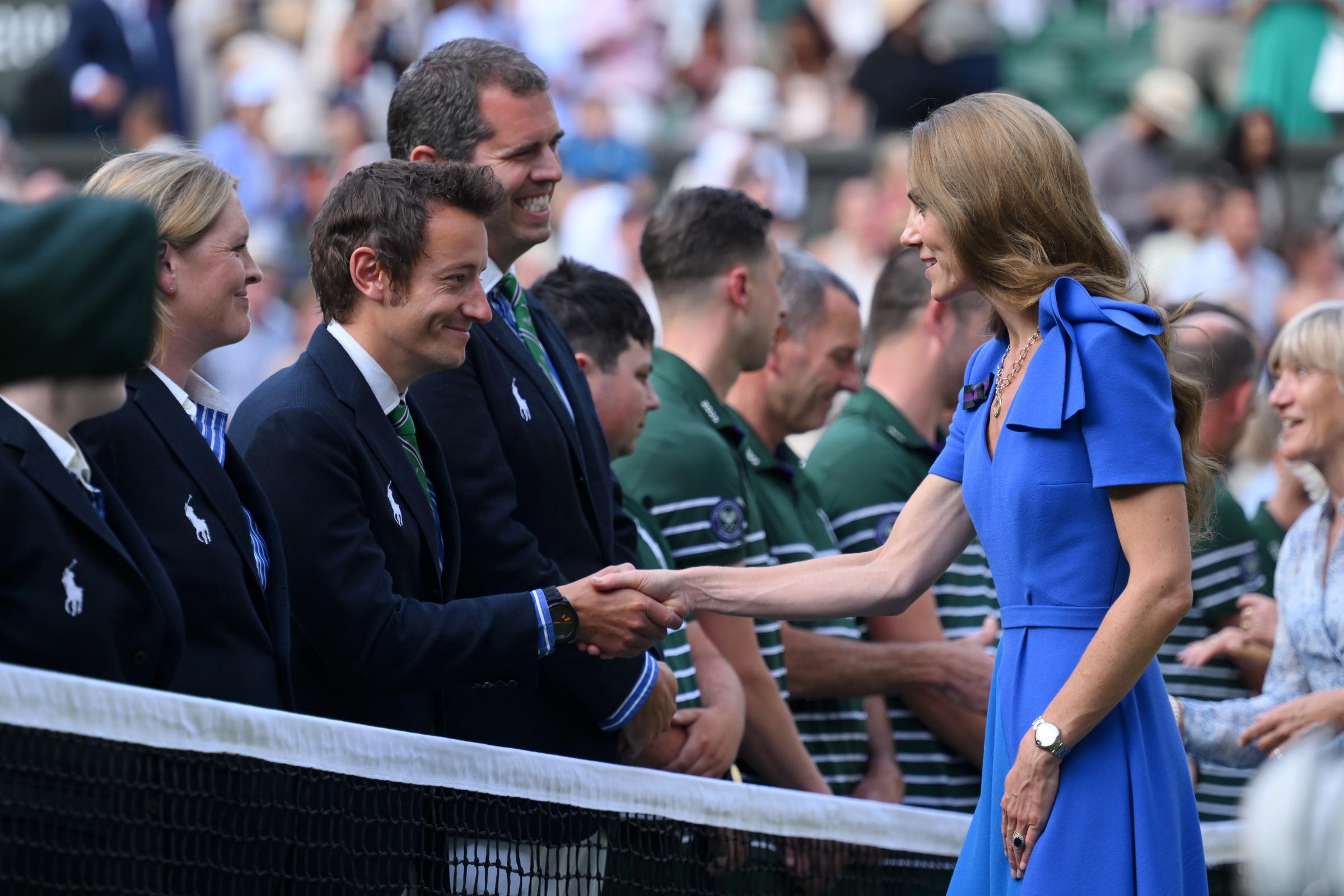 Princess Catherine greets members of the Wimbledon staff with a handshake near the court. She keeps her focus on each exchange as she moves down the line.