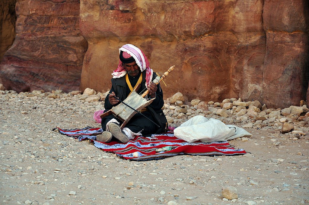 Jordanian bedouin man sit on a blanket in front of a mountain while playing a musical instrument on April 8 2010, in Petra, Jordan | Source Getty Images