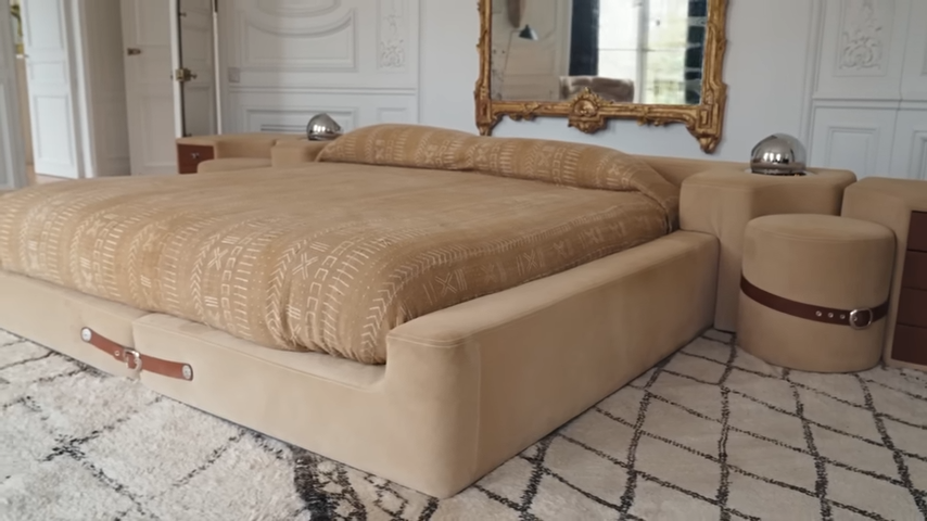 A close-up of the bespoke tan platform bed, showing off its unique leather belt straps and matching buckled suede bedside stools. | Source: YouTube/@Archdigest