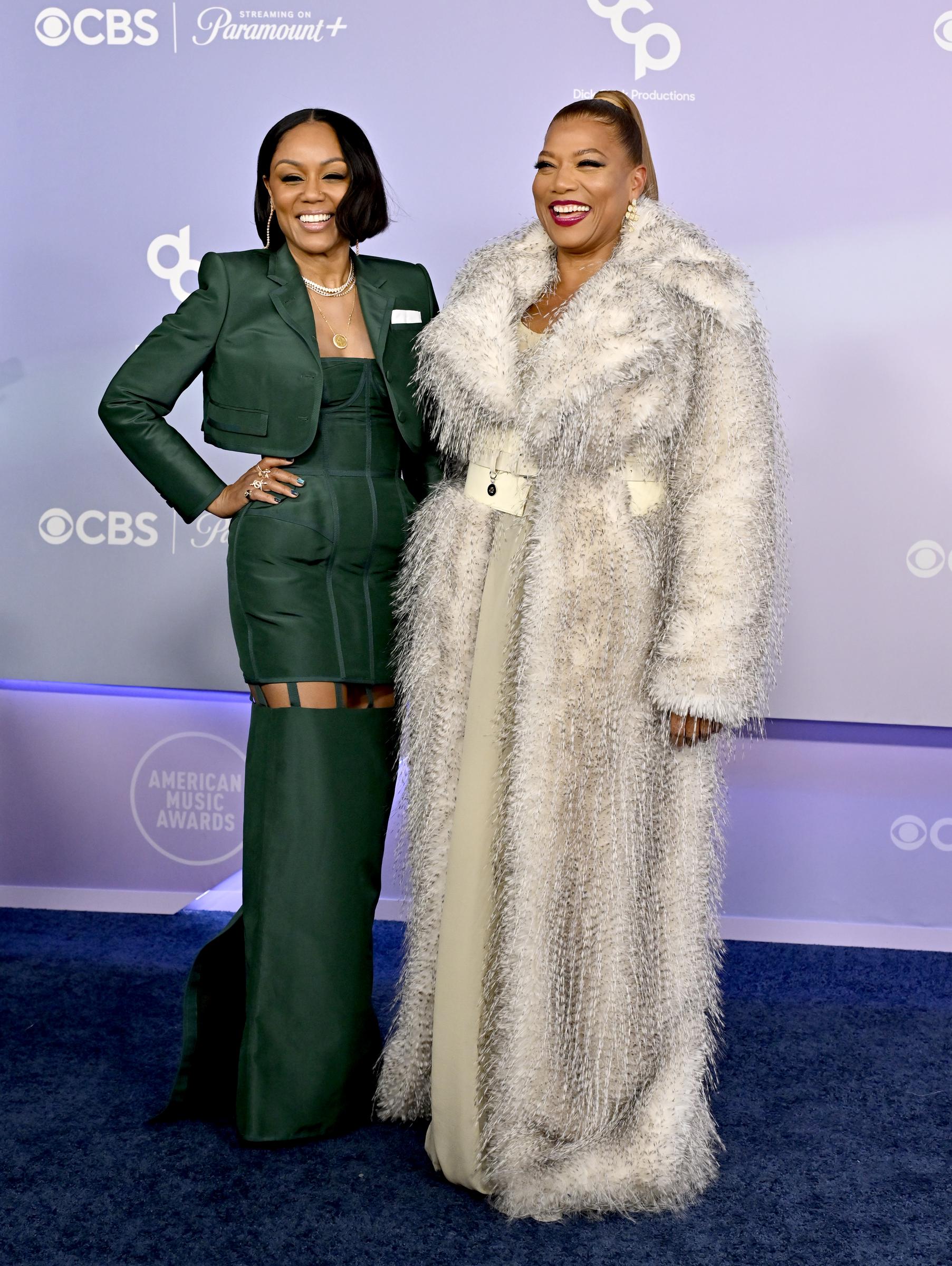 Eboni Nichols smiles confidently with one hand on her waist as Queen Latifah grins beside her during a polished pose for photographers at the AMAs.